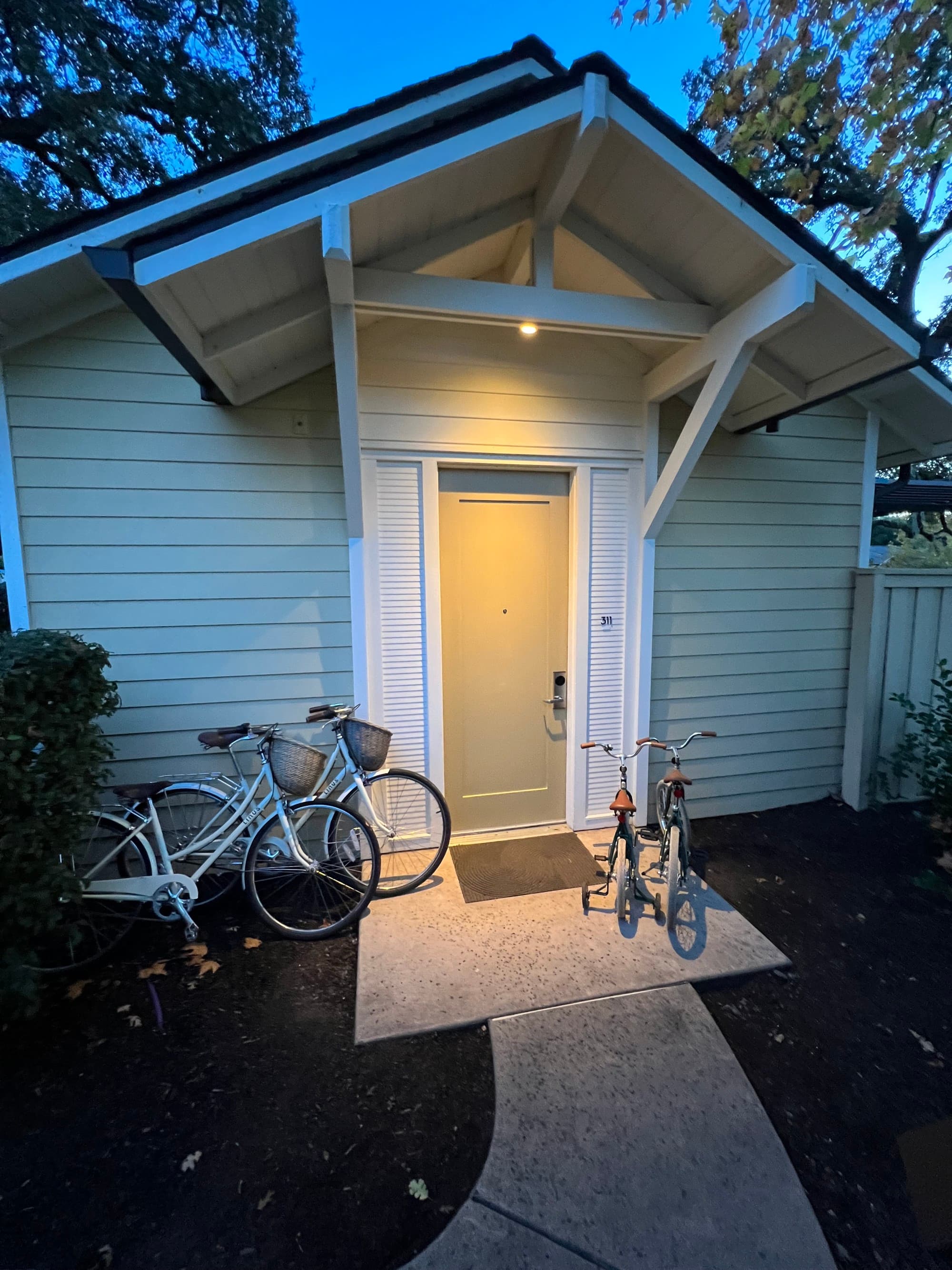 A white house with an illuminated yellow door and bikes on the front step.