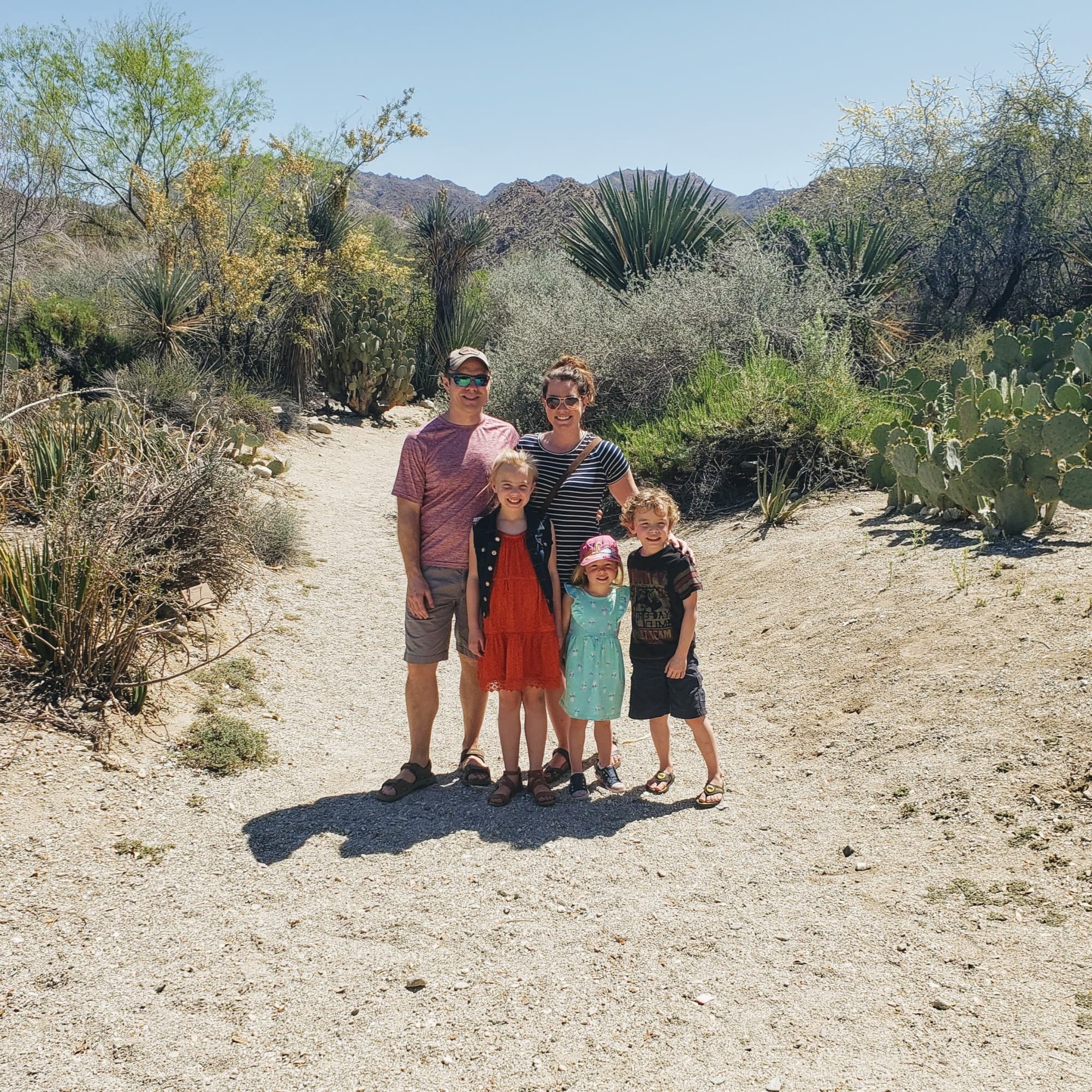 A family posing in a desert landscape on a bright sunny day surrounded by cactus, shrubs and other desert plants.