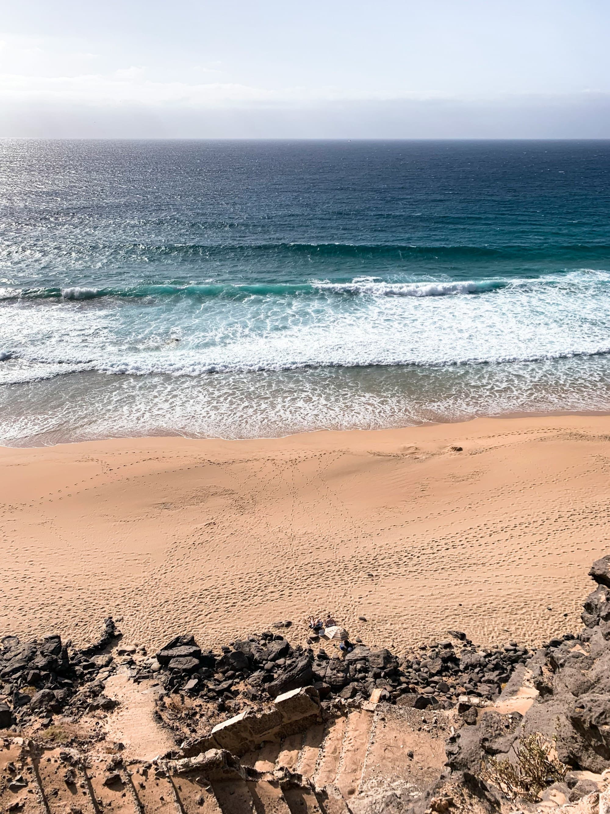 A view of a sandy beach with calm waves washing up on the shore during the day.