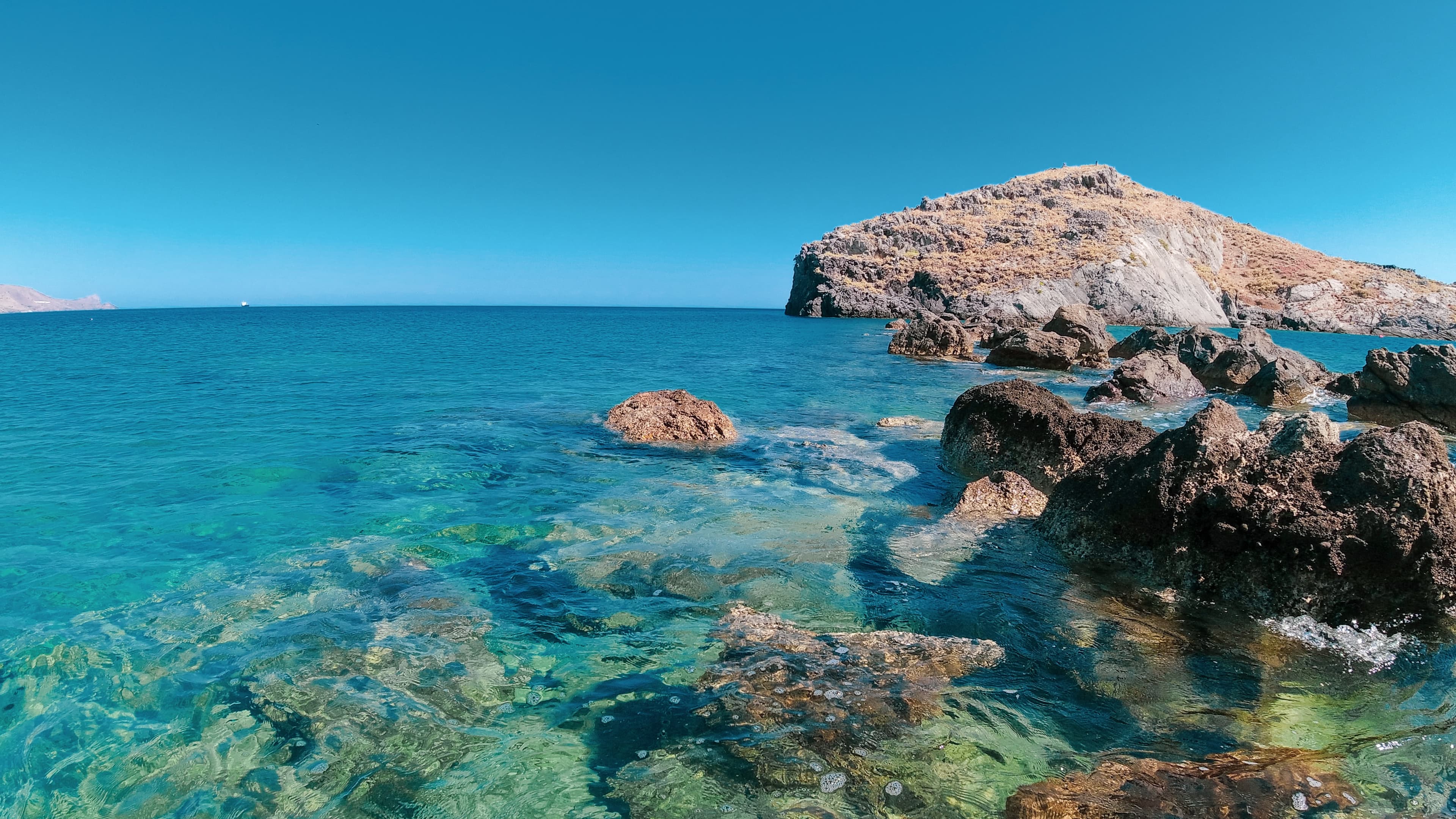 blue clear water with tan rocks and blue sky in Crete