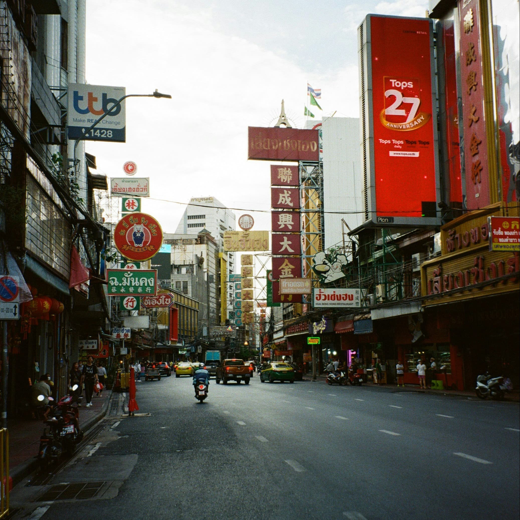 A bustling street scene with multilingual signage, vehicles, and buildings lining the road.