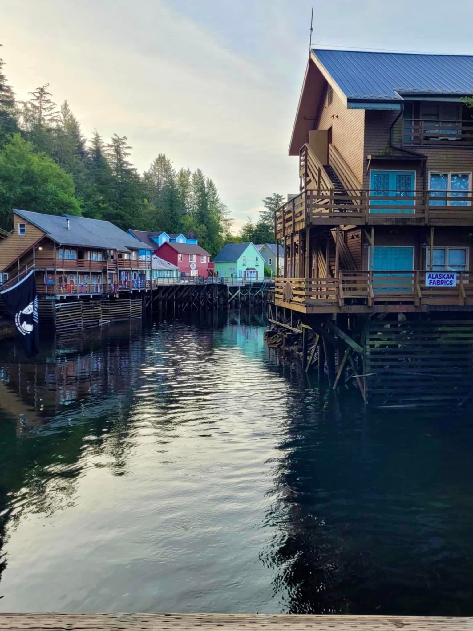 Brightly painted wooden buildings built over a body of water at Creek Street, Ketchikan at dusk.