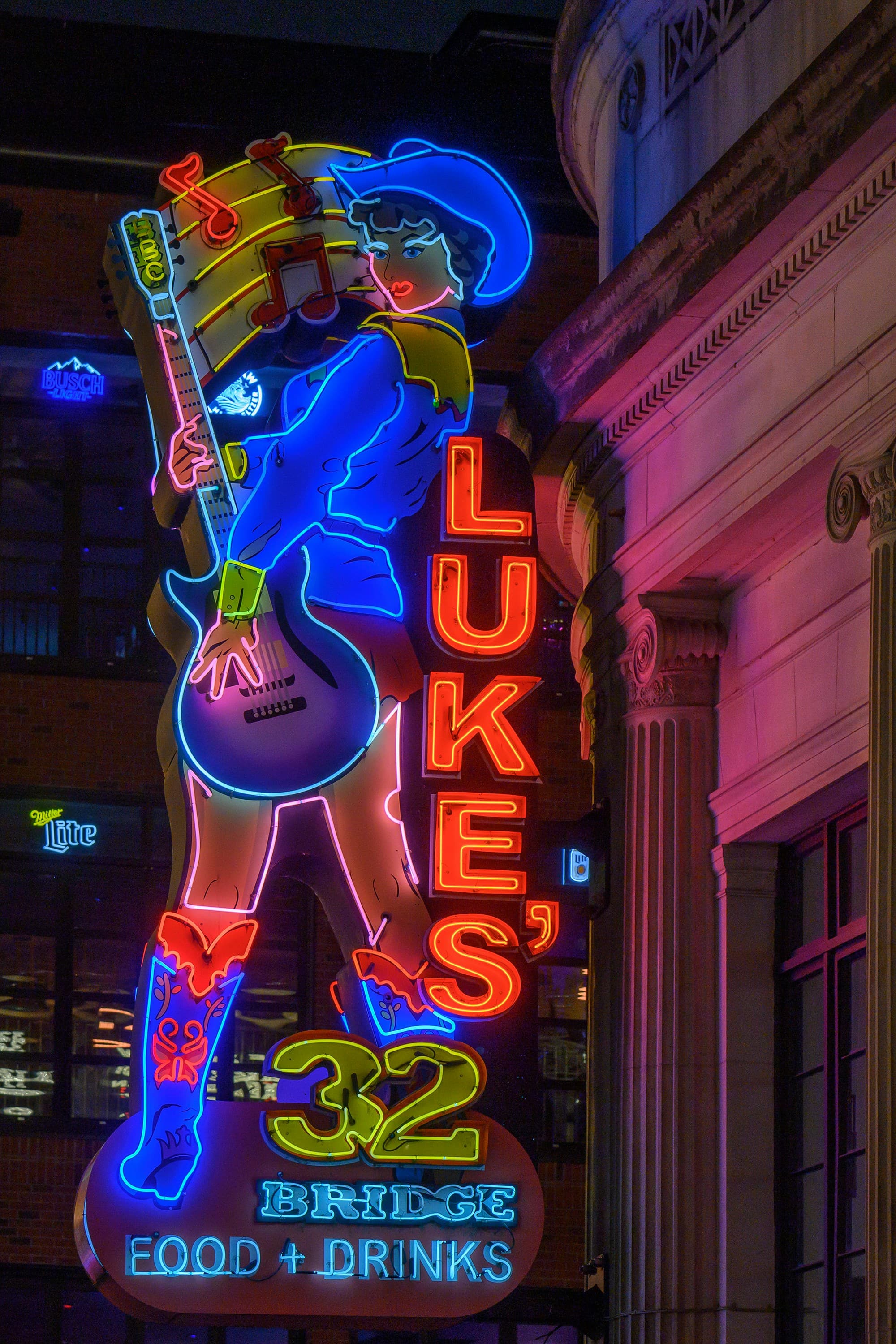 A neon sign with a woman wearing a cowboy hat and holding a guitar that reads "Lukes" at night.