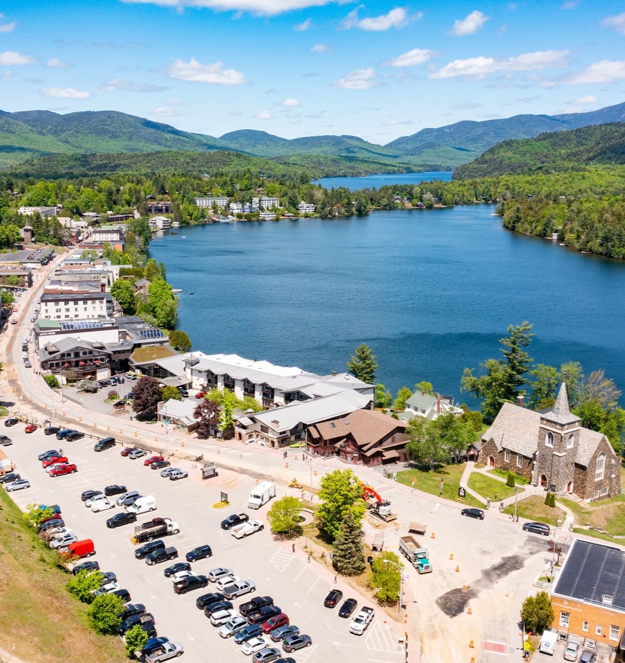 An aerial view of a large lake surrounded by trees and hills with a parking lot in the foreground