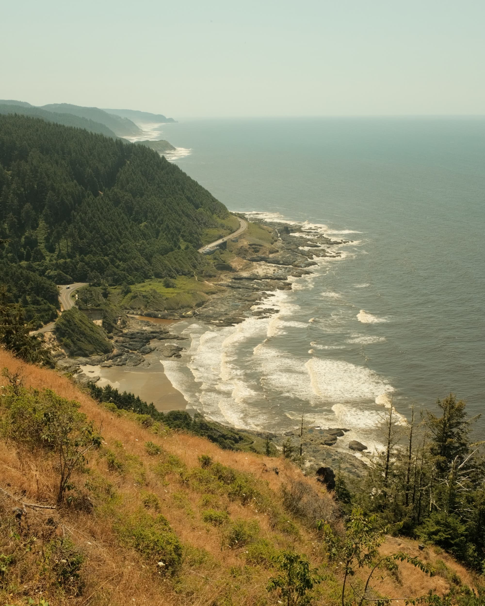 A scenic coastal view with a winding road beside rocky shores and crashing waves.