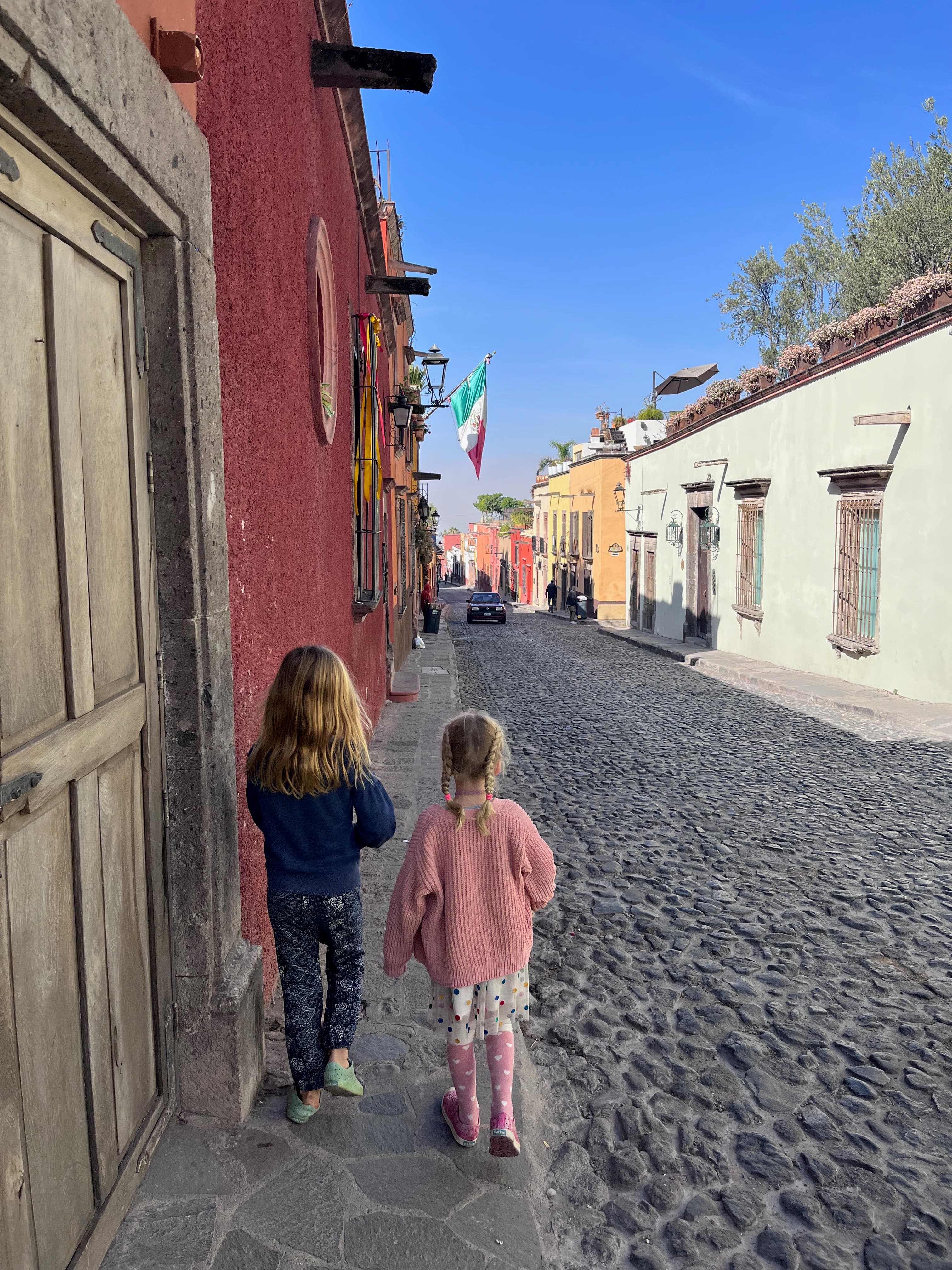 Two children walking down a street with a cobble stone road