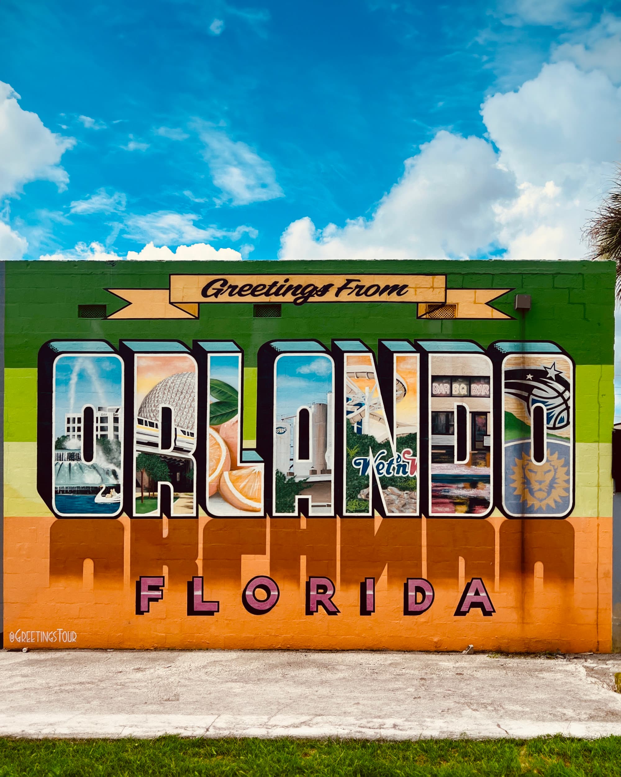 Signage saying "Greetings From Orlando" against a clear blue sky dotted with wispy clouds.