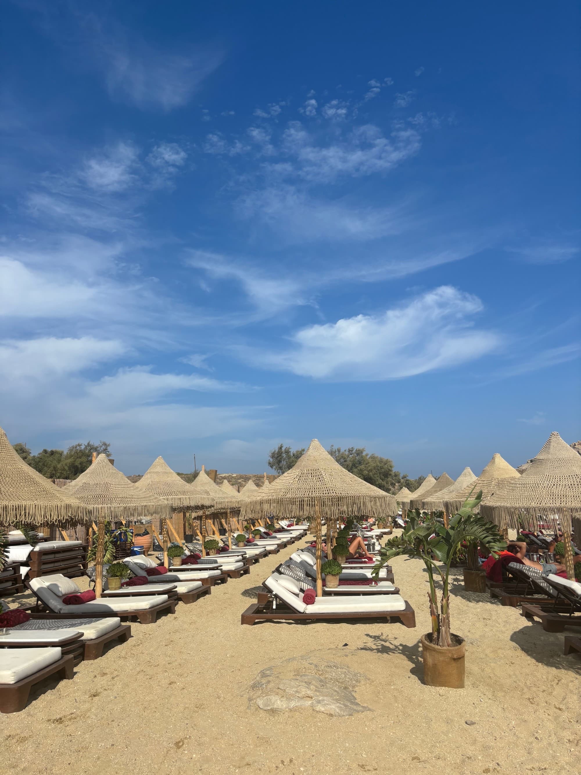 Covered daybeds on the beach beneath a blue sky with wispy clouds.