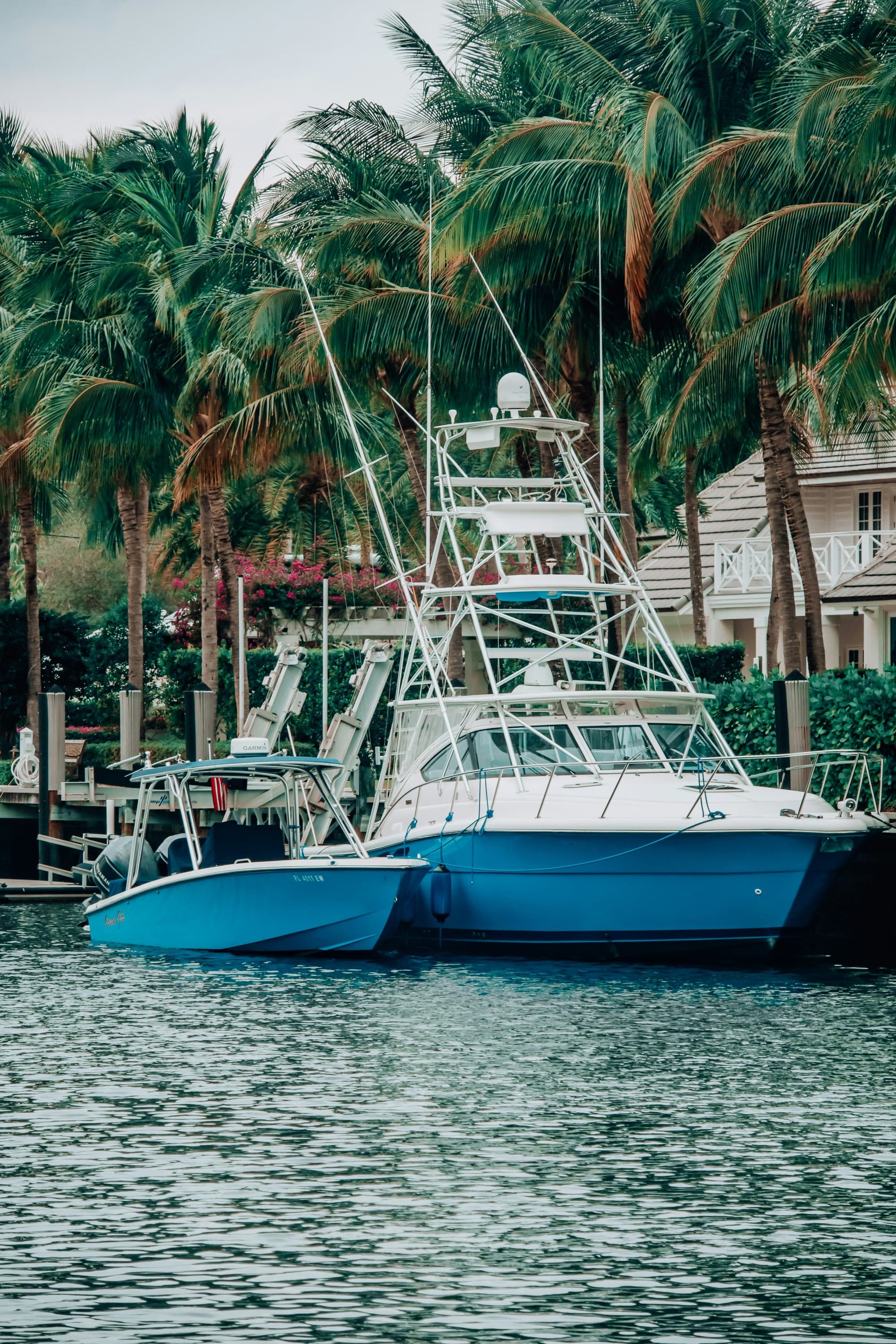 A blue and white sport fishing boat docked in calm waters with palm trees in the background.