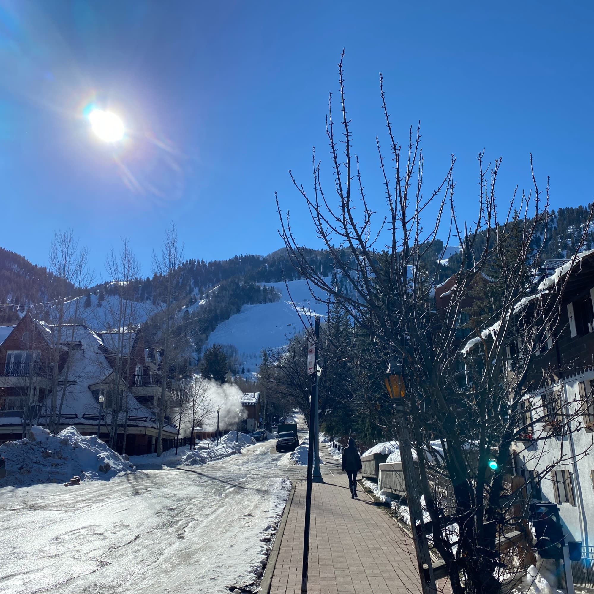 Snow covered road in front of buildings and a mountain in the distance.