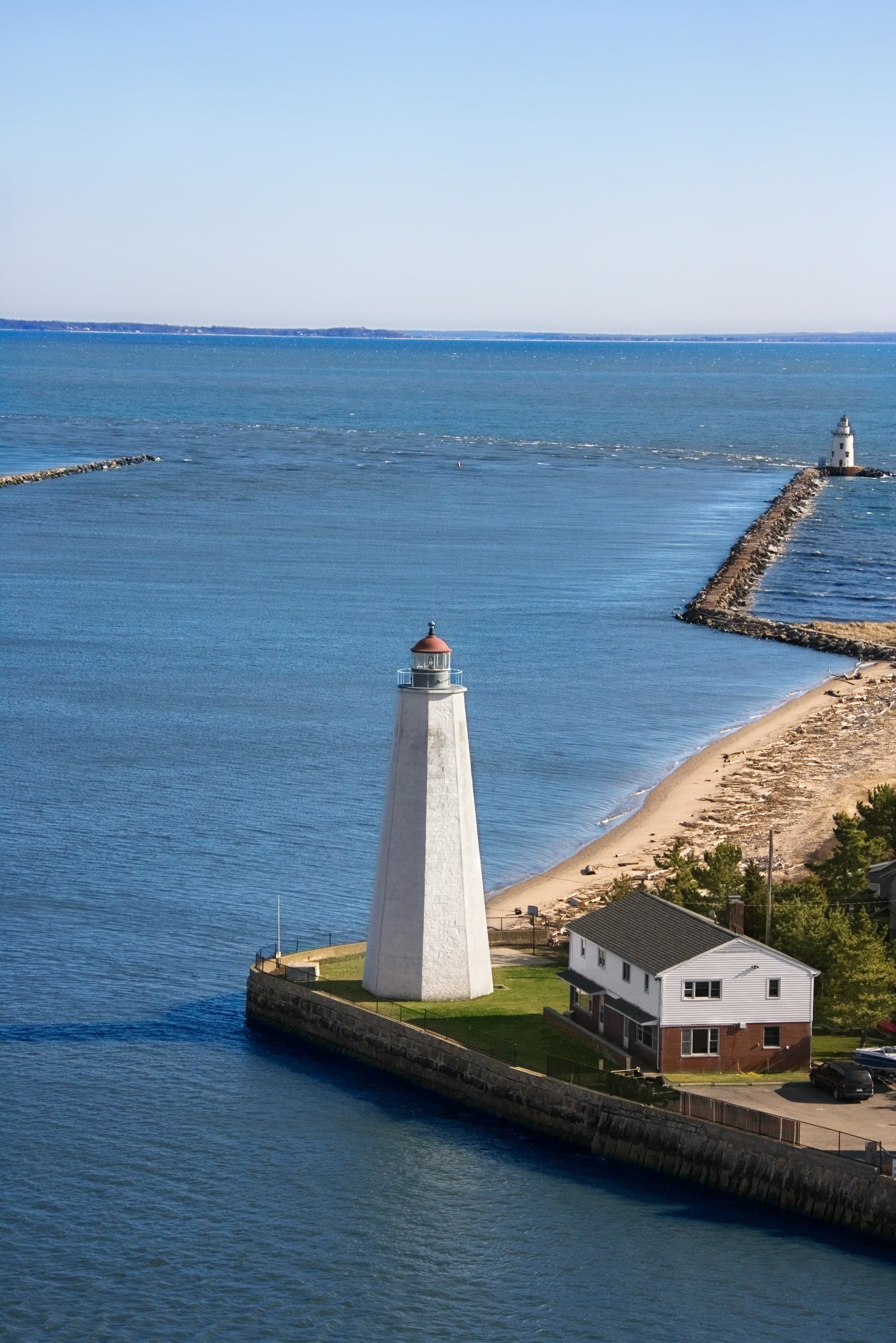 A lighthouse stands tall on a narrow strip of land between two bodies of water under a clear blue sky.