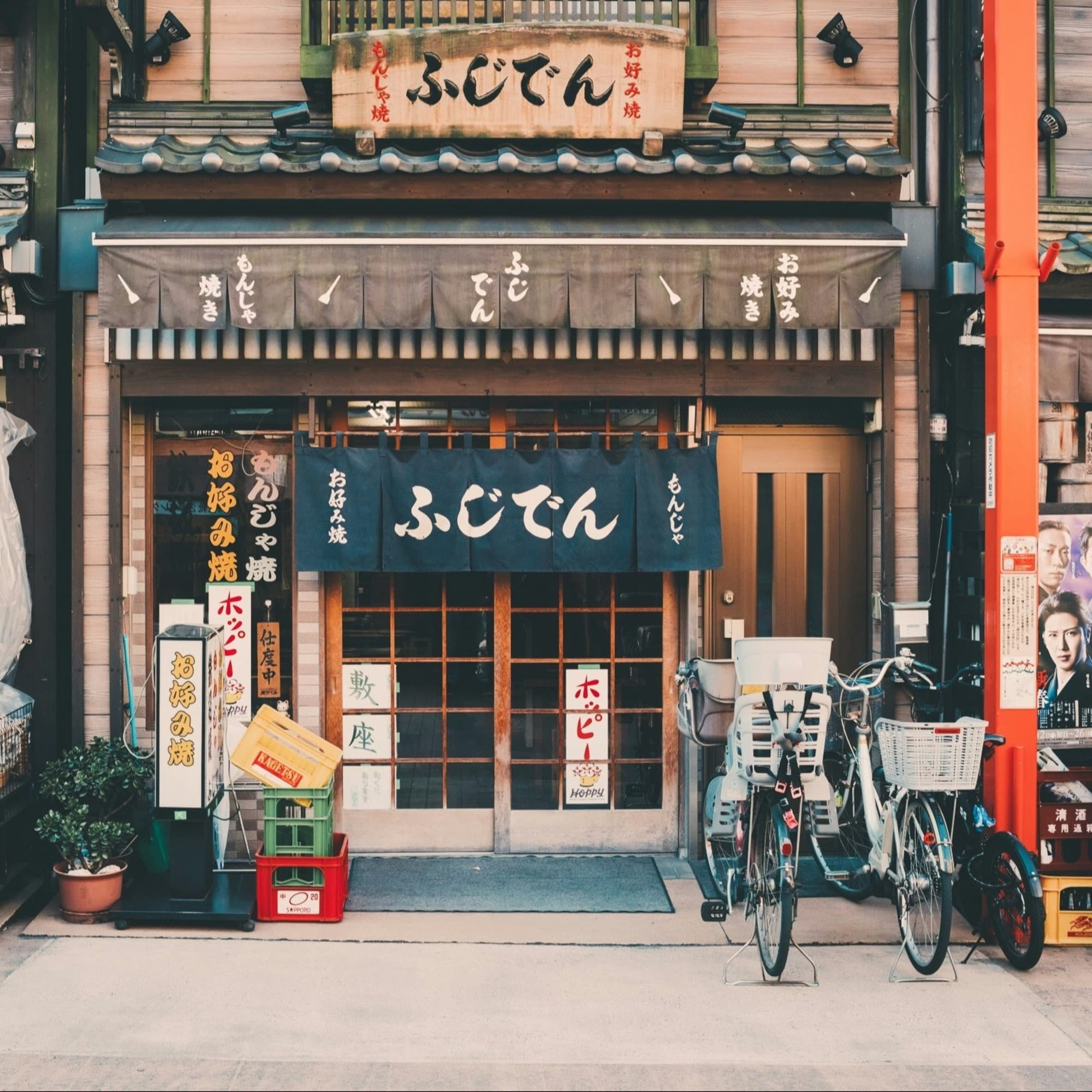 The image shows a traditional Japanese storefront with signage and bicycles parked in front.