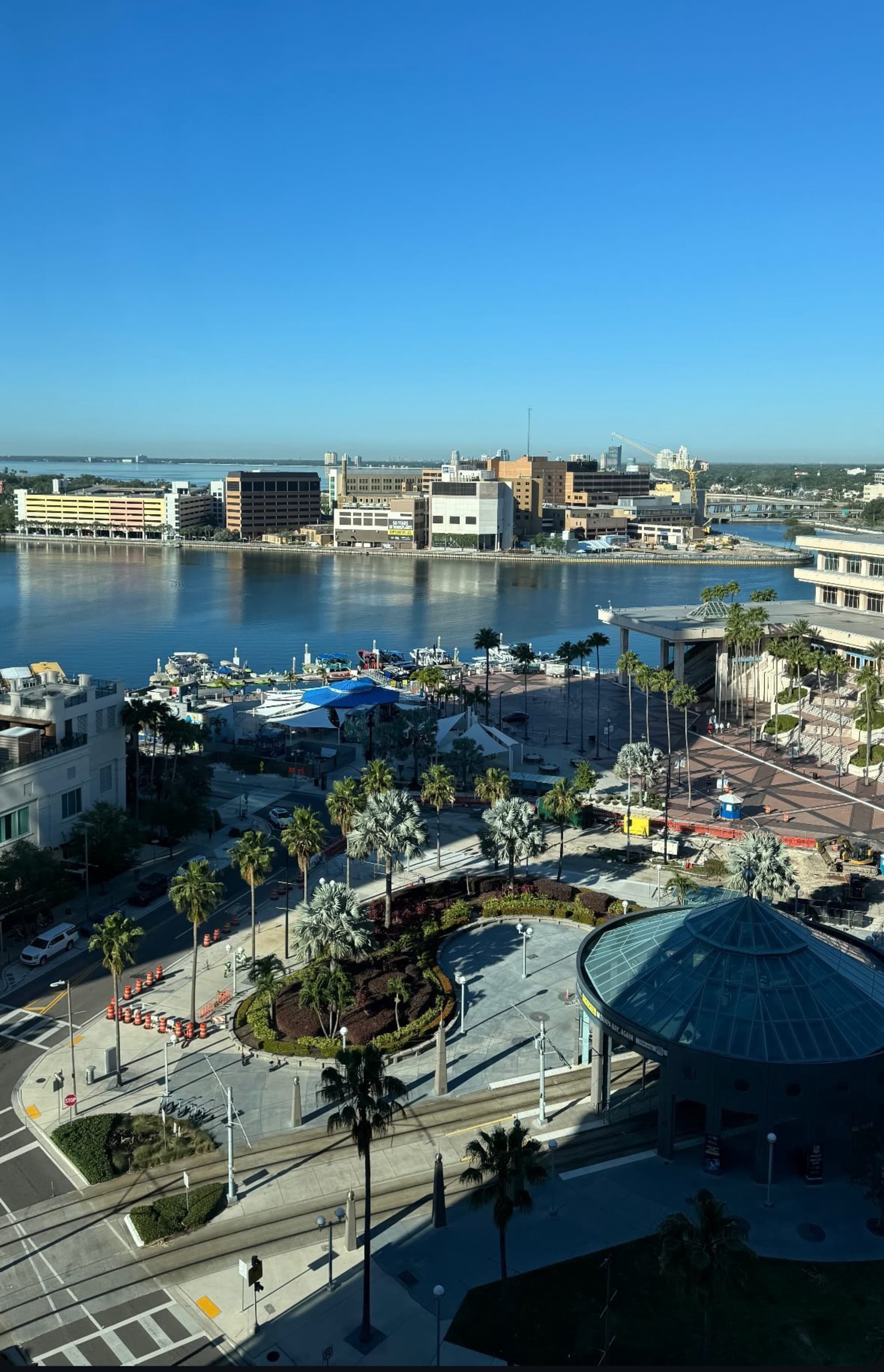 A coastal cityscape with buildings, roads, and a marina under a clear blue sky.