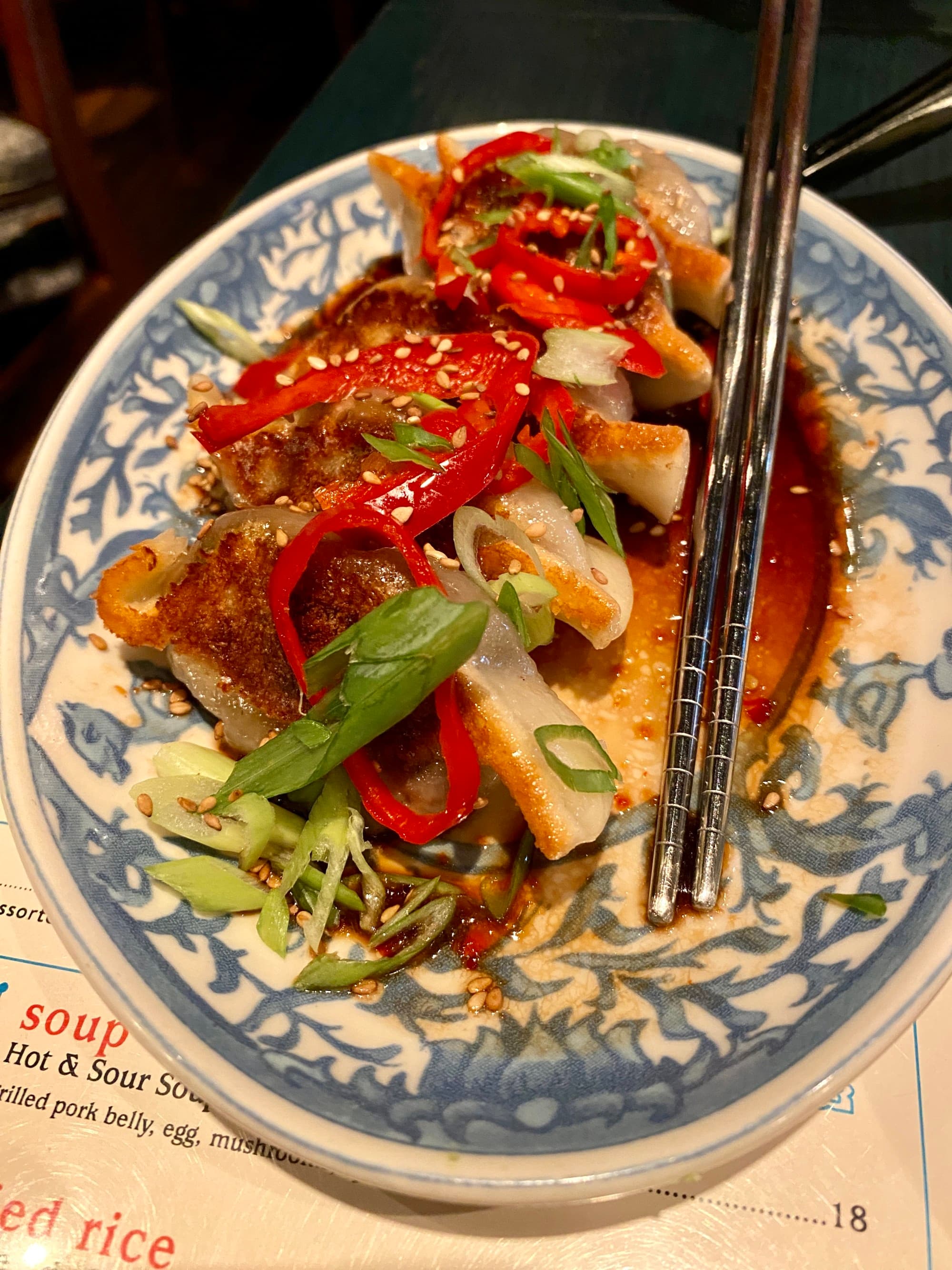 Food on a blue and white patterned plate with a pair of metal chopsticks sitting on top