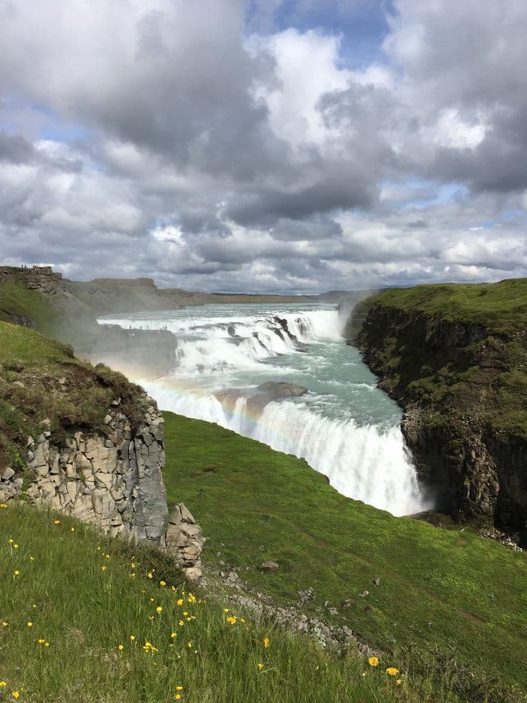 A vast waterfall next to grass-covered hills during the daytime