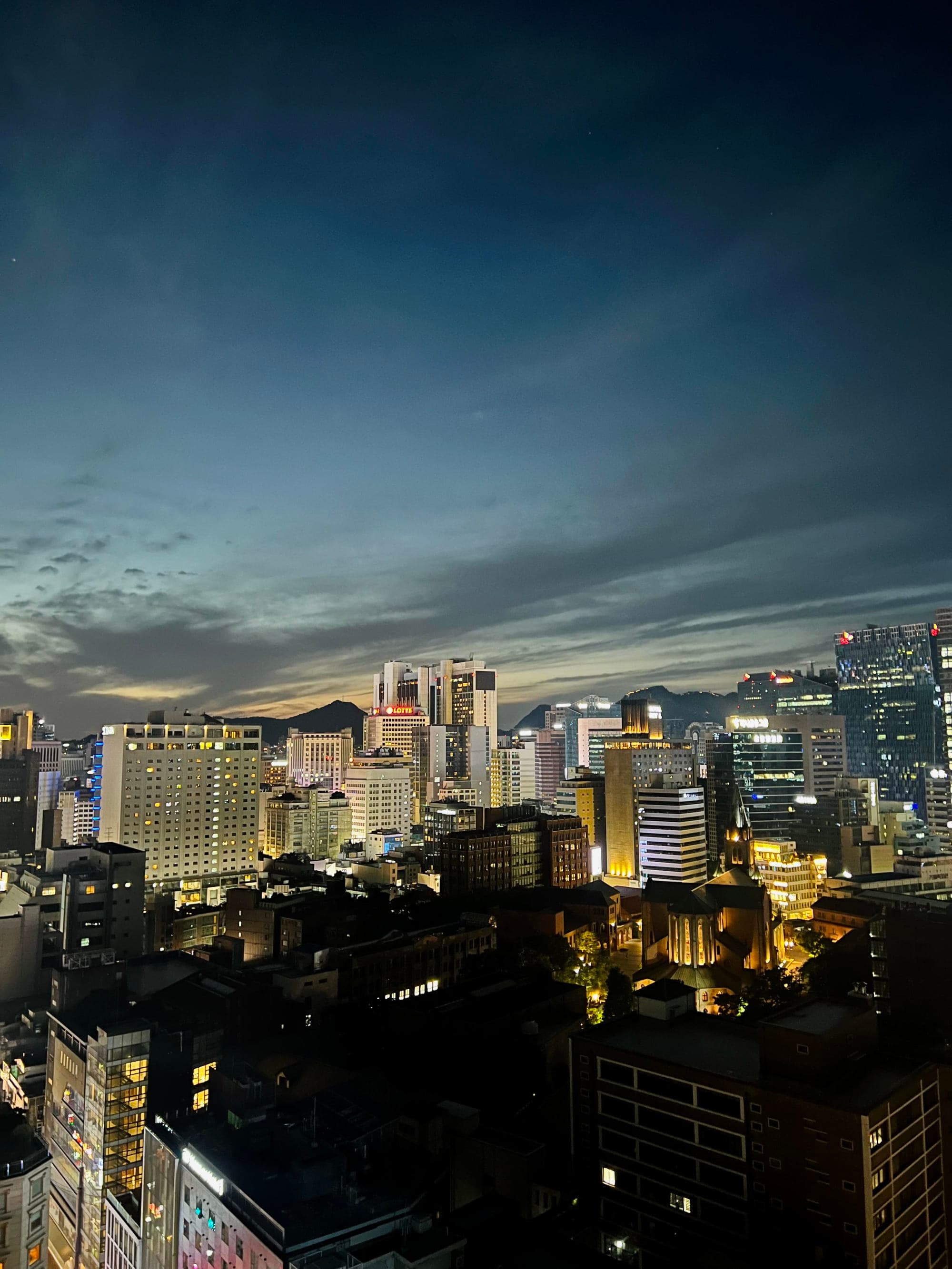 The image depicts a nighttime cityscape with illuminated buildings under a dusky sky.