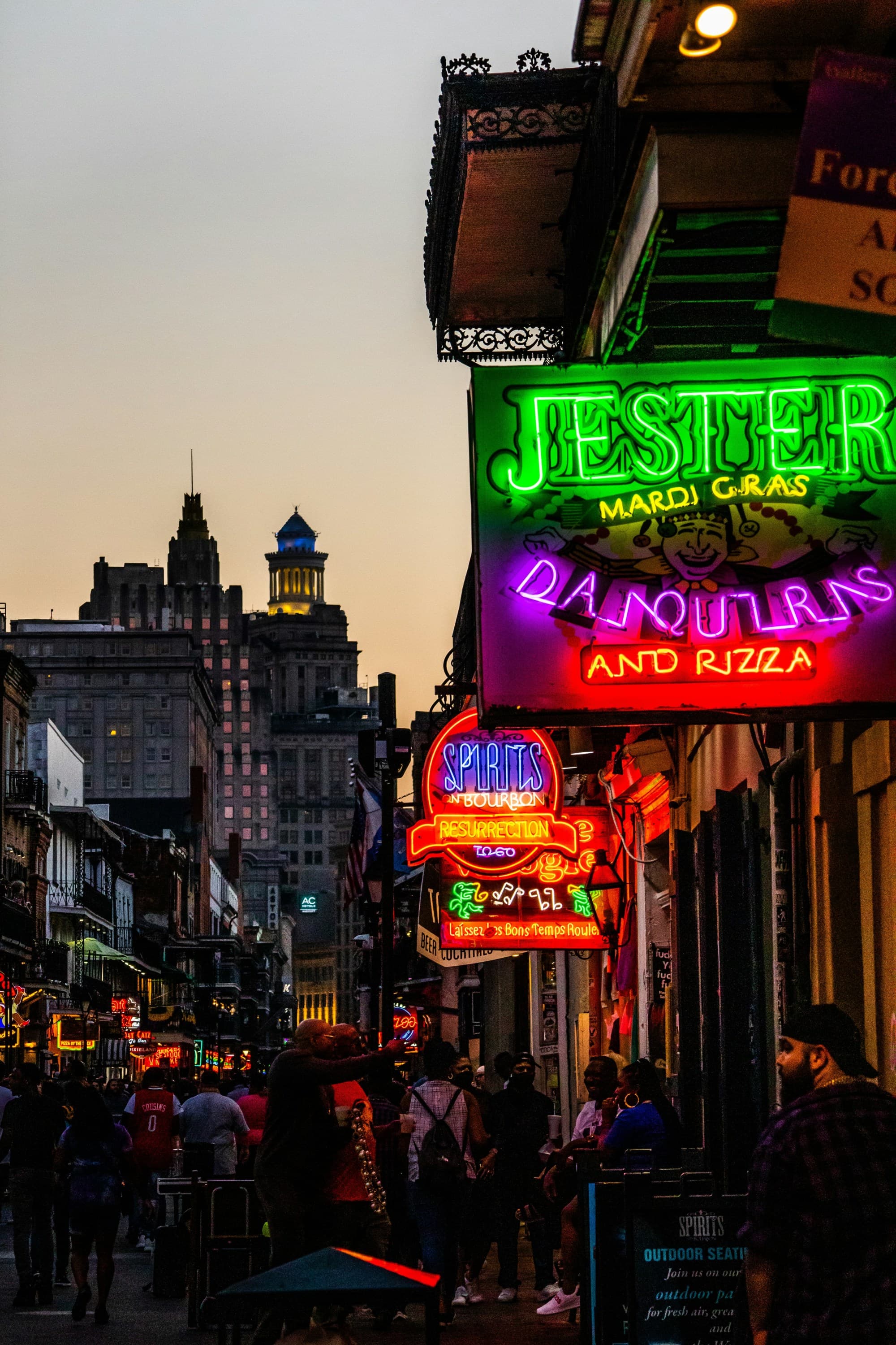 A city street at nighttime with neon signs glowing and people walking around outside