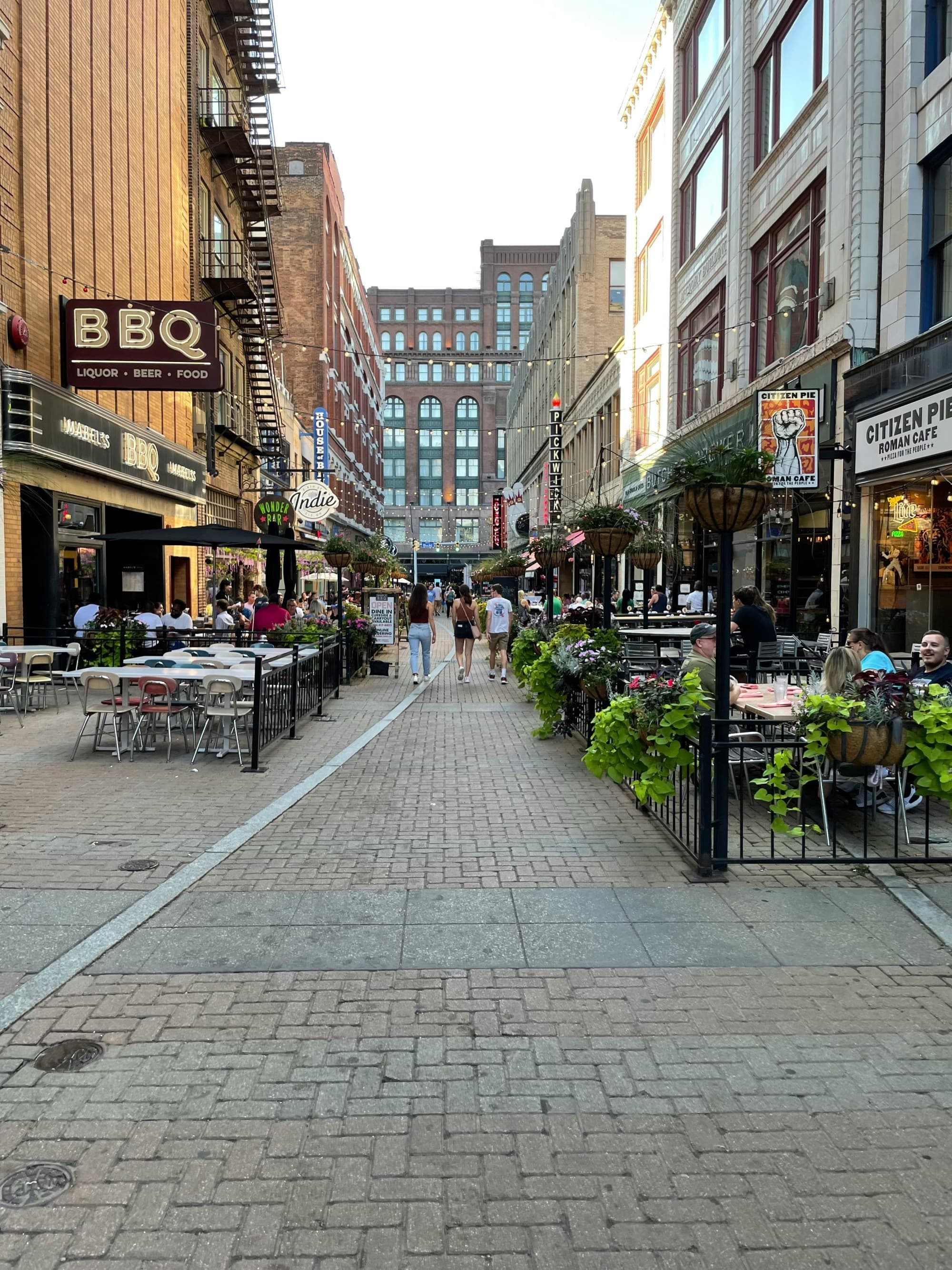 An urban street scene with outdoor dining, pedestrians, and multi-story buildings.