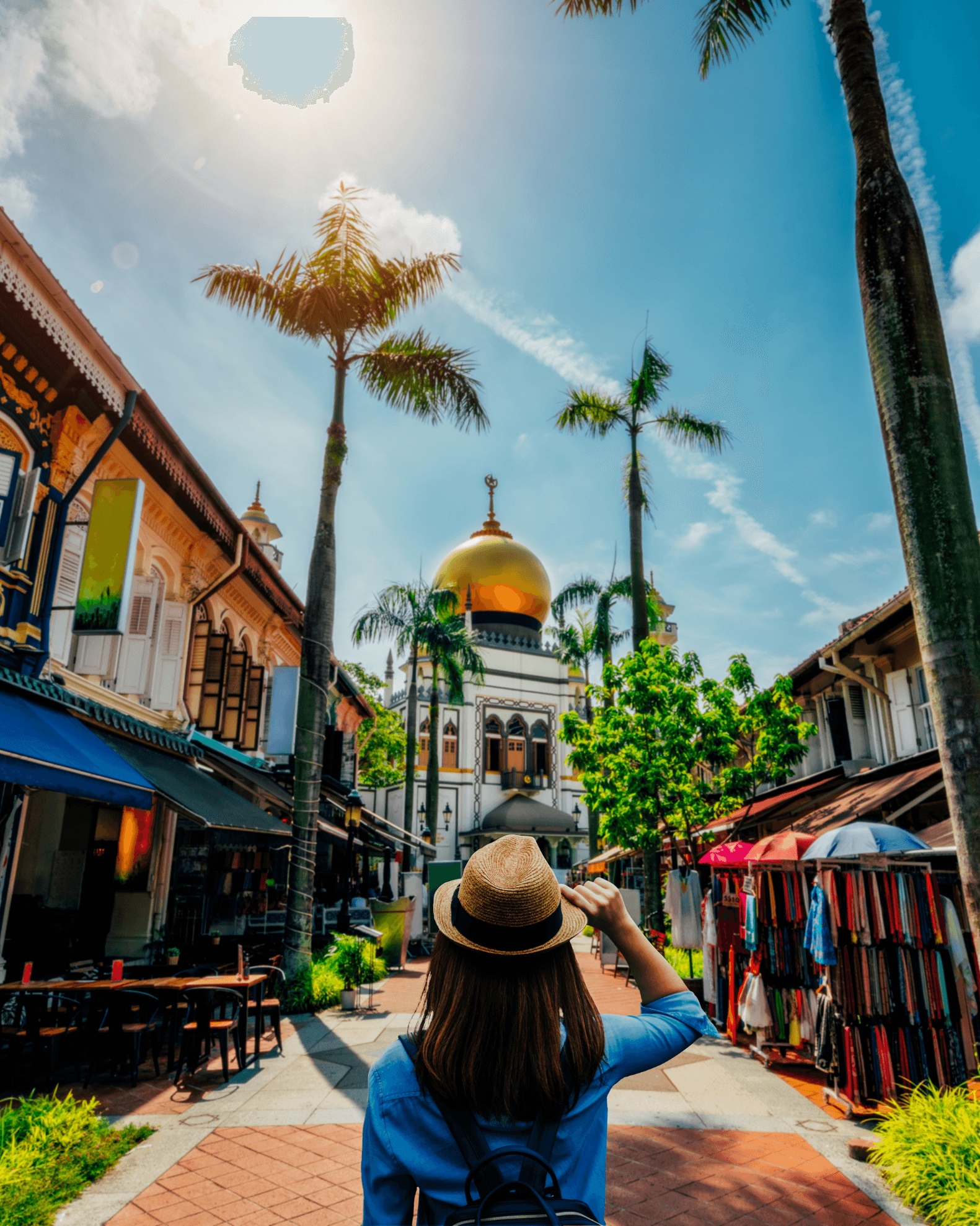 Woman on a street with shops and palm trees on either side and a large building with a golden dome in front.