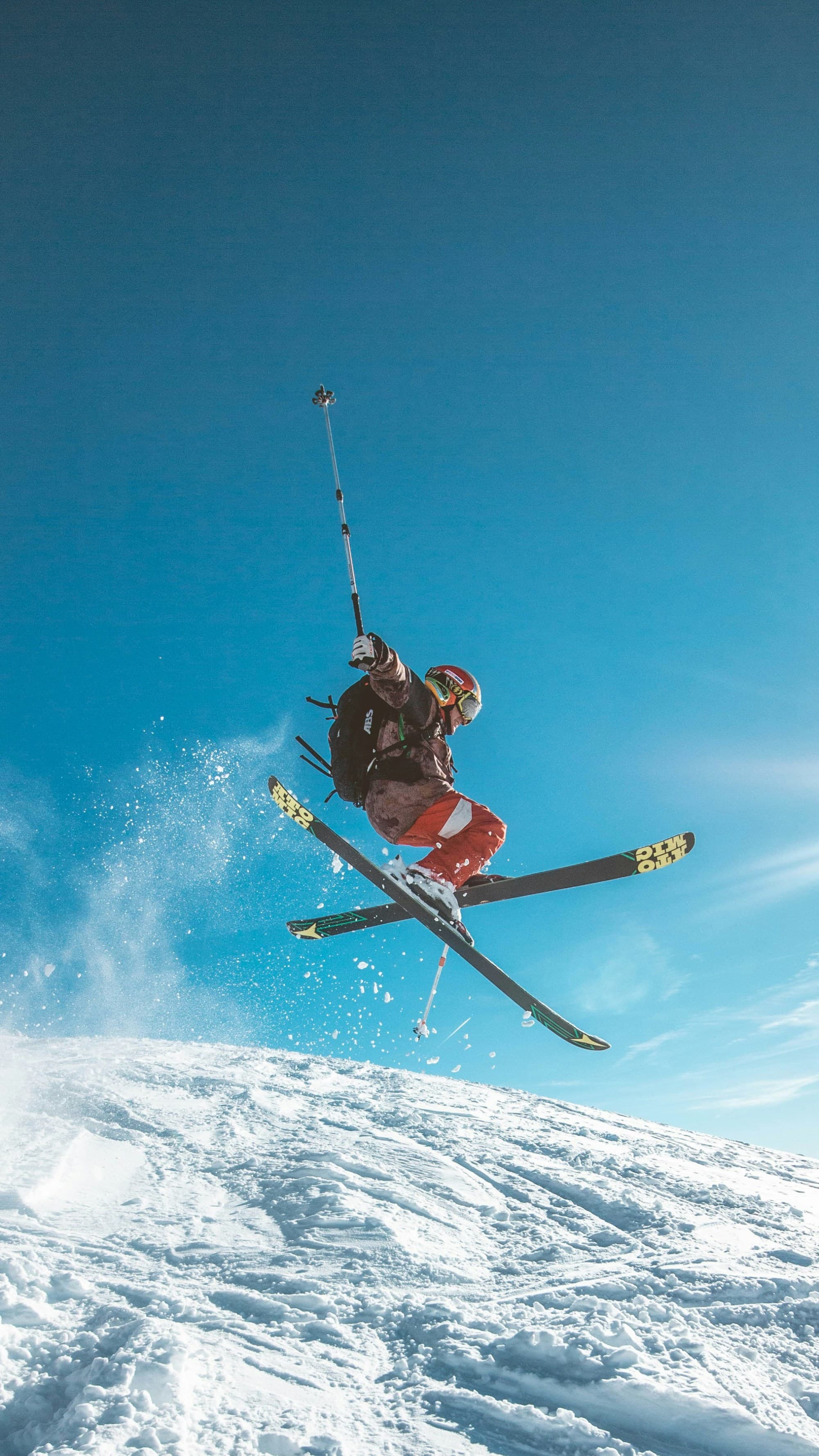 A skier goes off a jump with a blue sky behind.