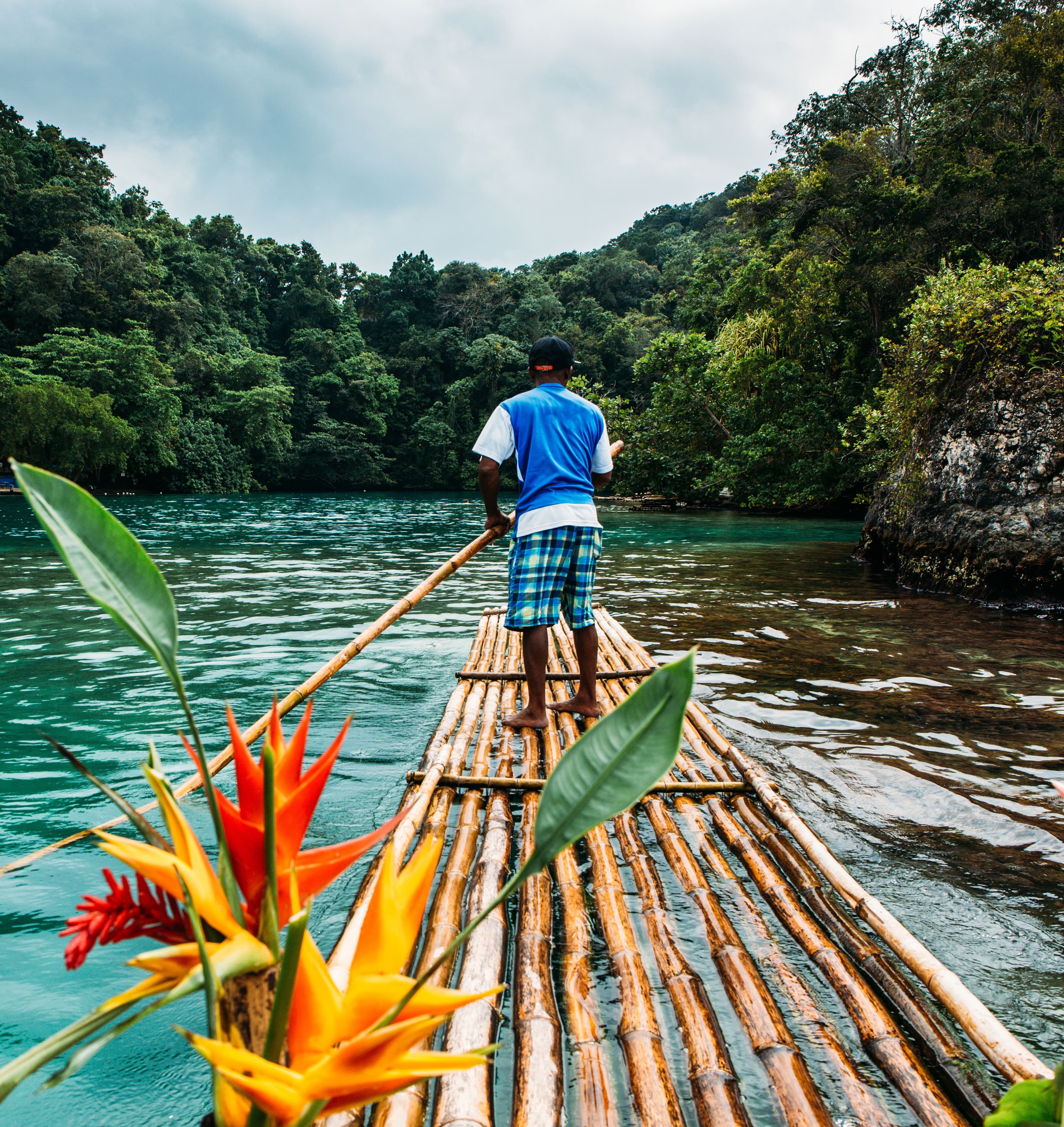 A person rowing a river raft down a body of water between a lush forest