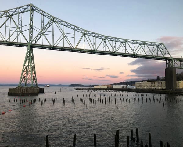 A green truss bridge over a body of water during the evening.