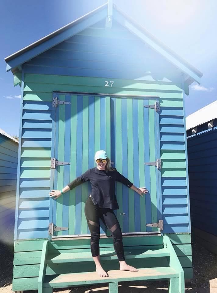 A woman posing in front of a blue green cabin.