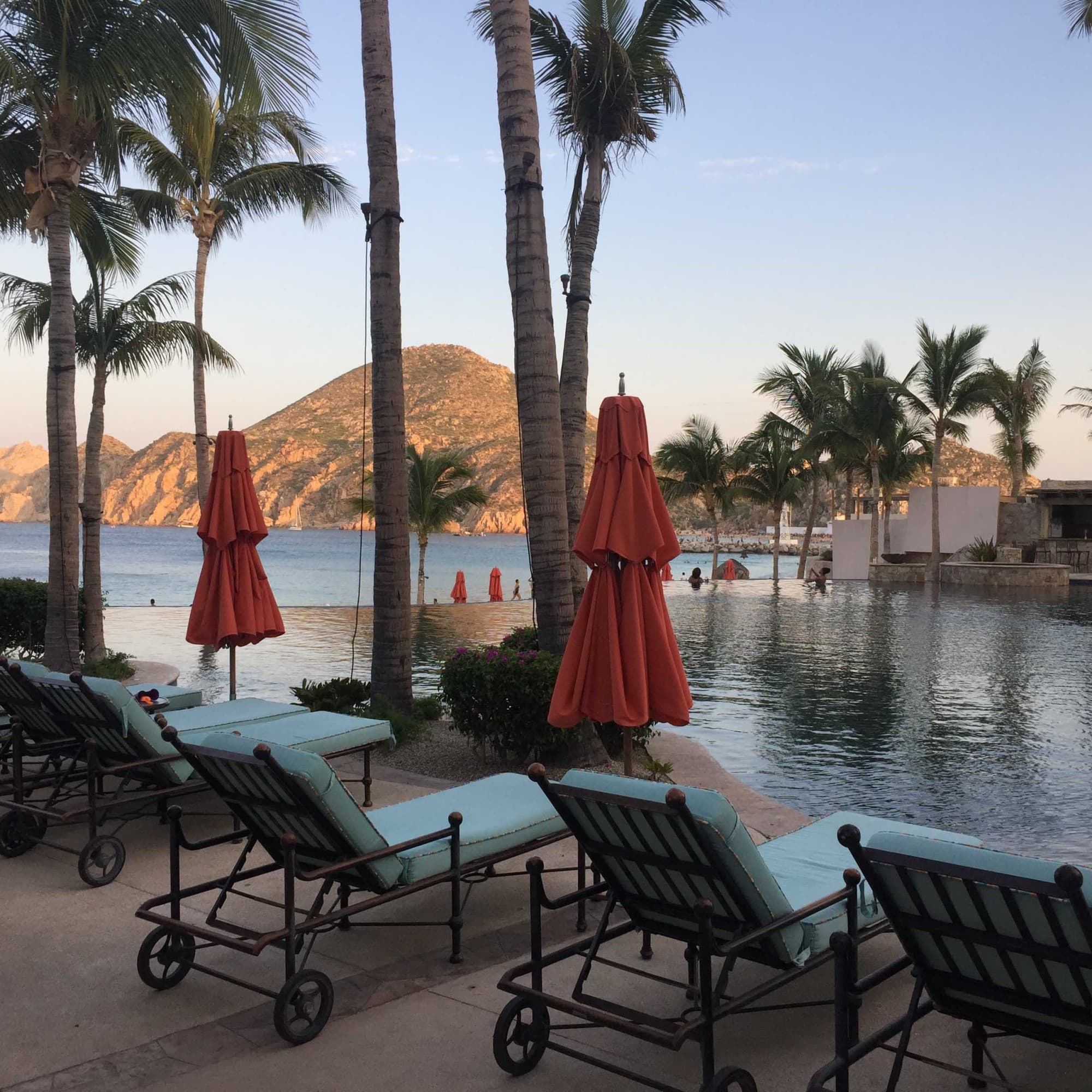 Lounging chairs and red umbrellas near a pool area in a resort.