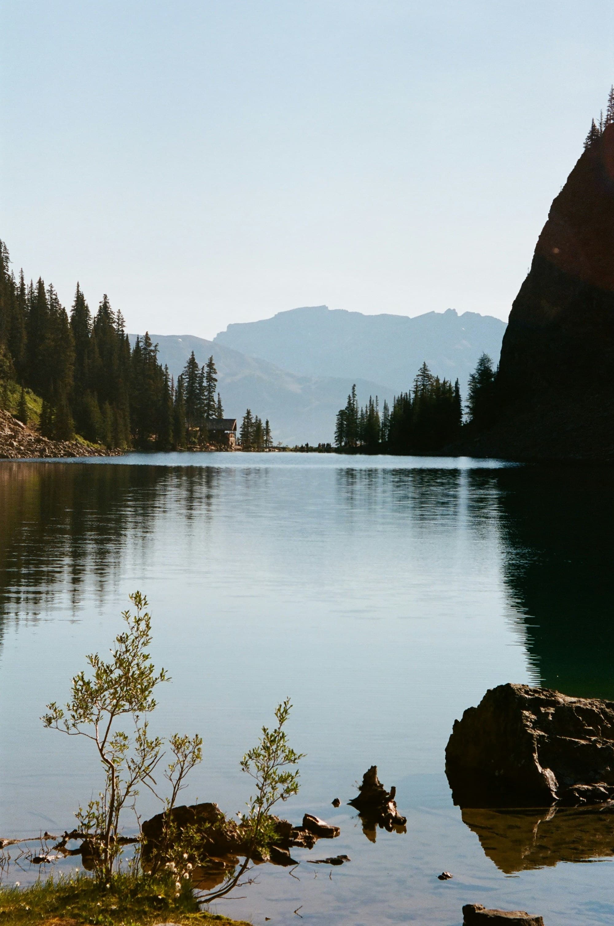 The image shows a mountain lake surrounded by trees and rocky terrain under a clear sky.