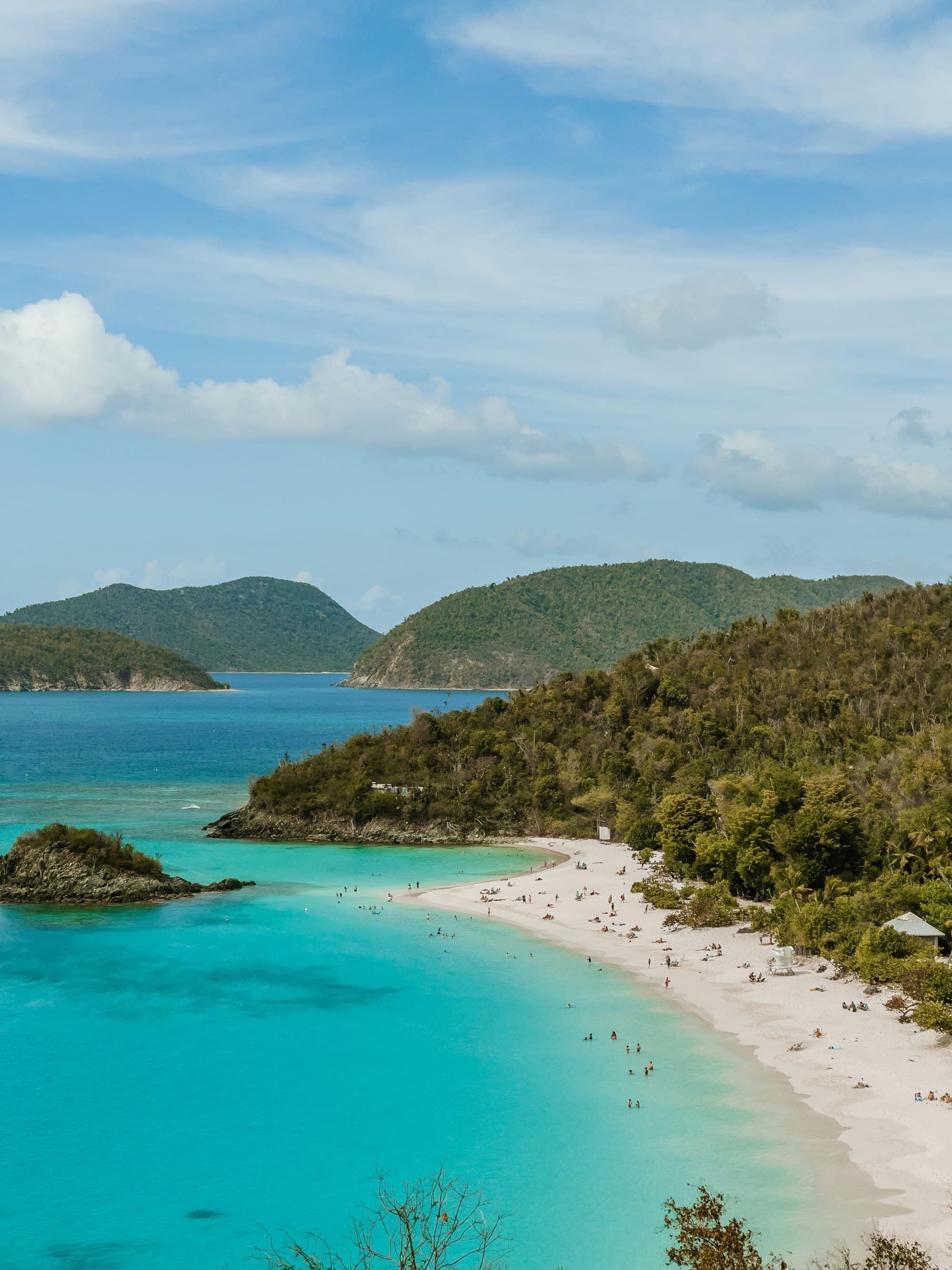 A beautiful turquoise beach with people, surrounded by lush greenery and hills under a clear blue sky.