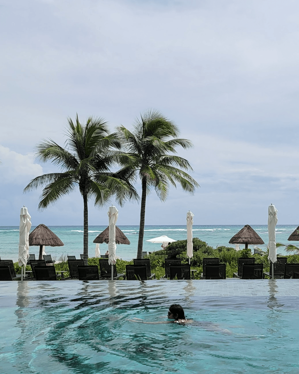 A view of the sunset at Conrad Tulum as the sun dips below the ocean horizon as palm trees sway in the breeze.