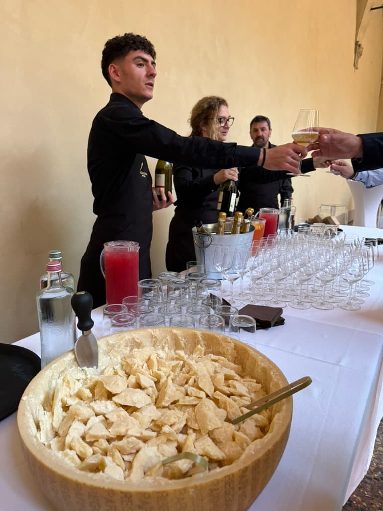 A long table with a large bowl of Parmesan chunks on one end and servers serving drinks.