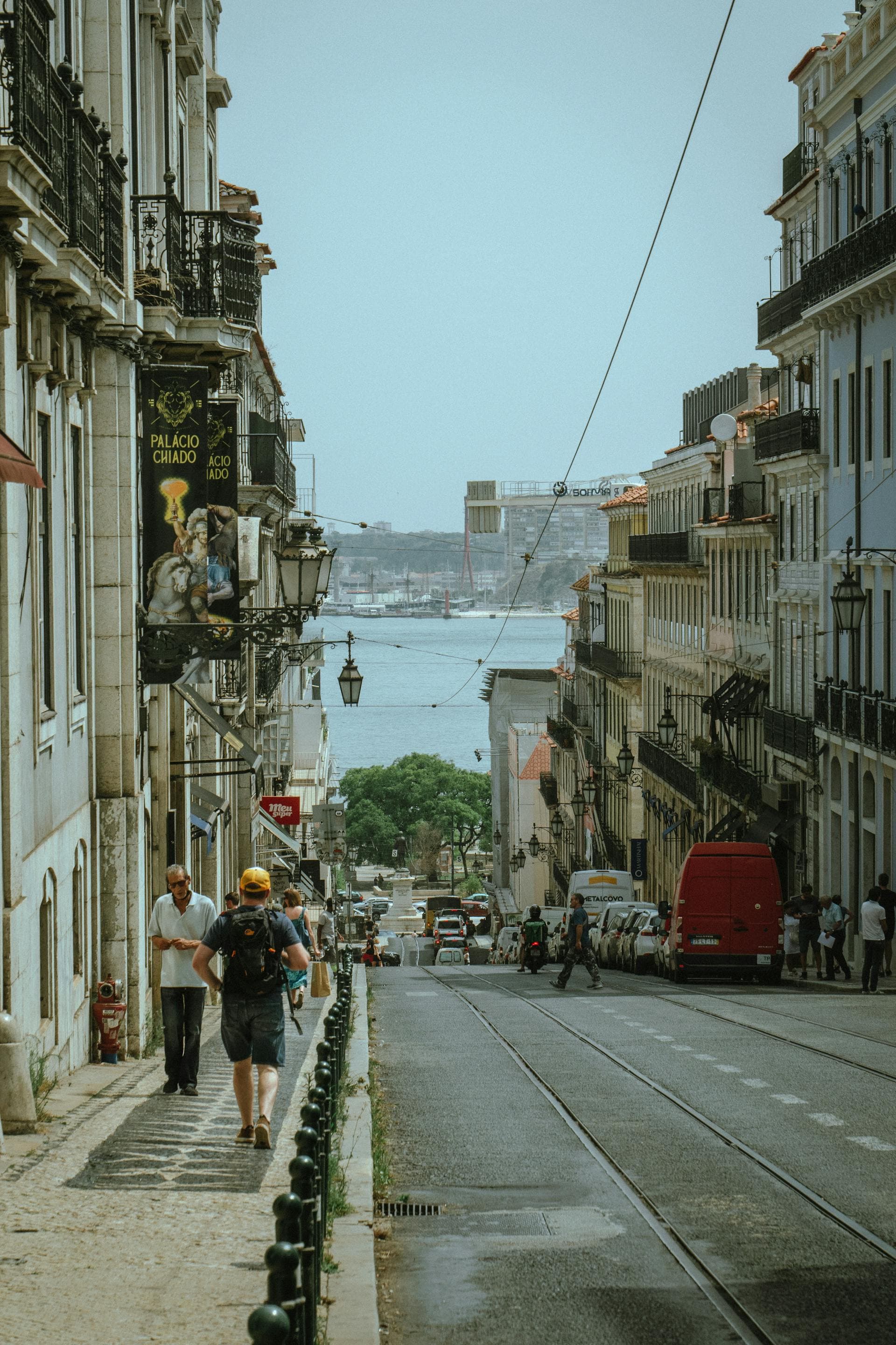 A bustling street corner in Lisbon overlooks the water on a clear day.