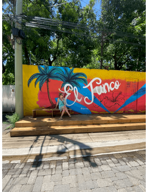 One of the many bright street murals lining the main road in El Tunco under lush foliage on a sunny day.