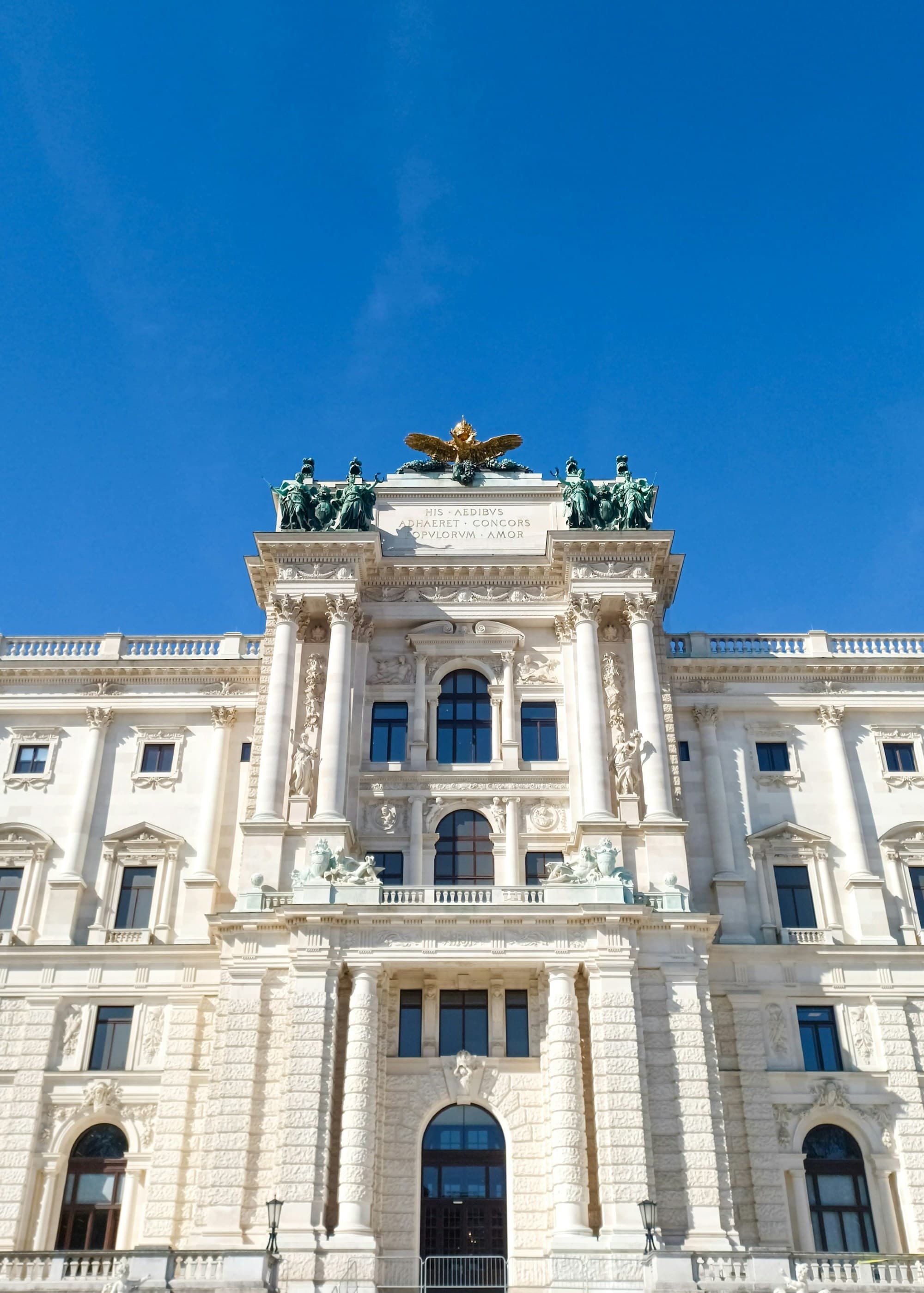 A view looking up at a white two story building with pillars and statues on top during the day.