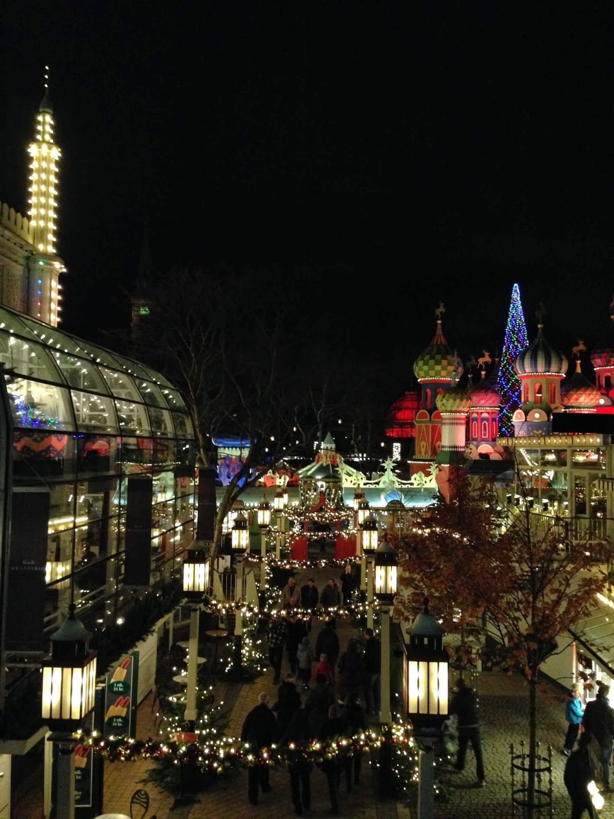 A vibrant night-time scene of an outdoor market or fair with illuminated buildings and festive lights.