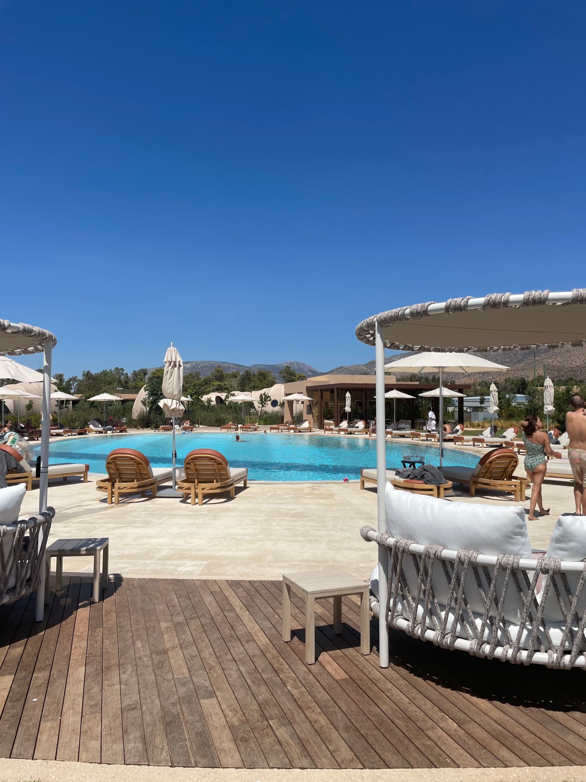 An outdoor pool area with sun loungers, umbrellas, and a clear blue sky suggests a leisure or vacation setting.