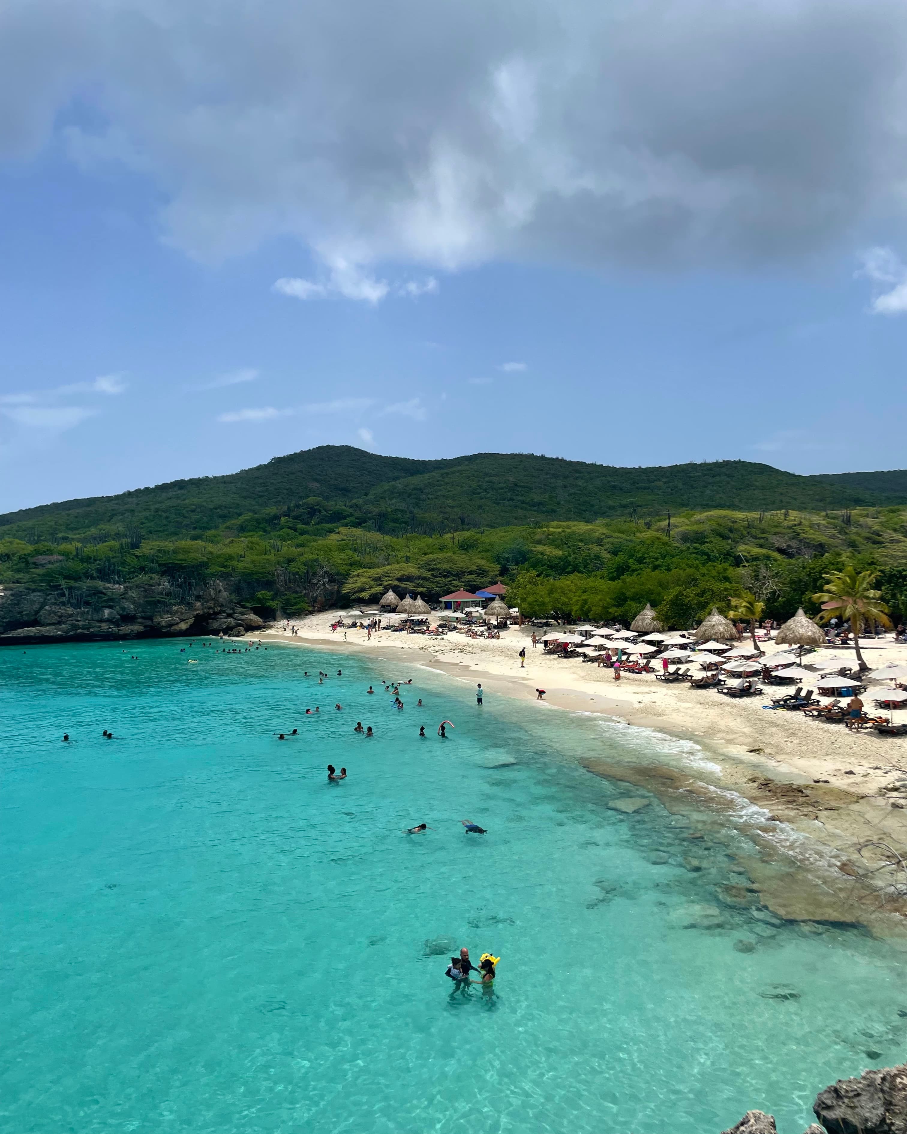 Beach with clear blue water and lounge chairs on the sand.