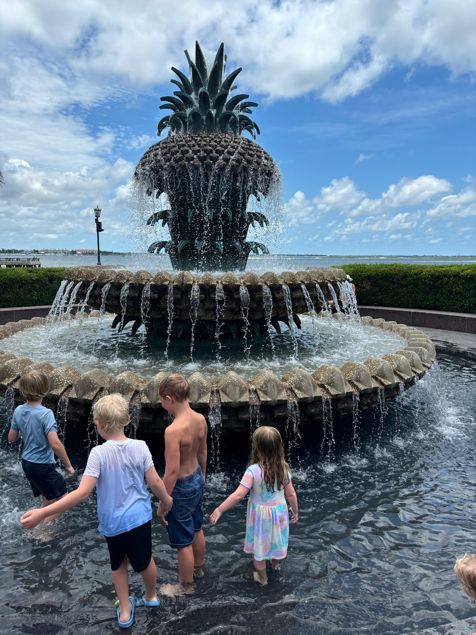 Kids playing around pineapple shaped fountain.