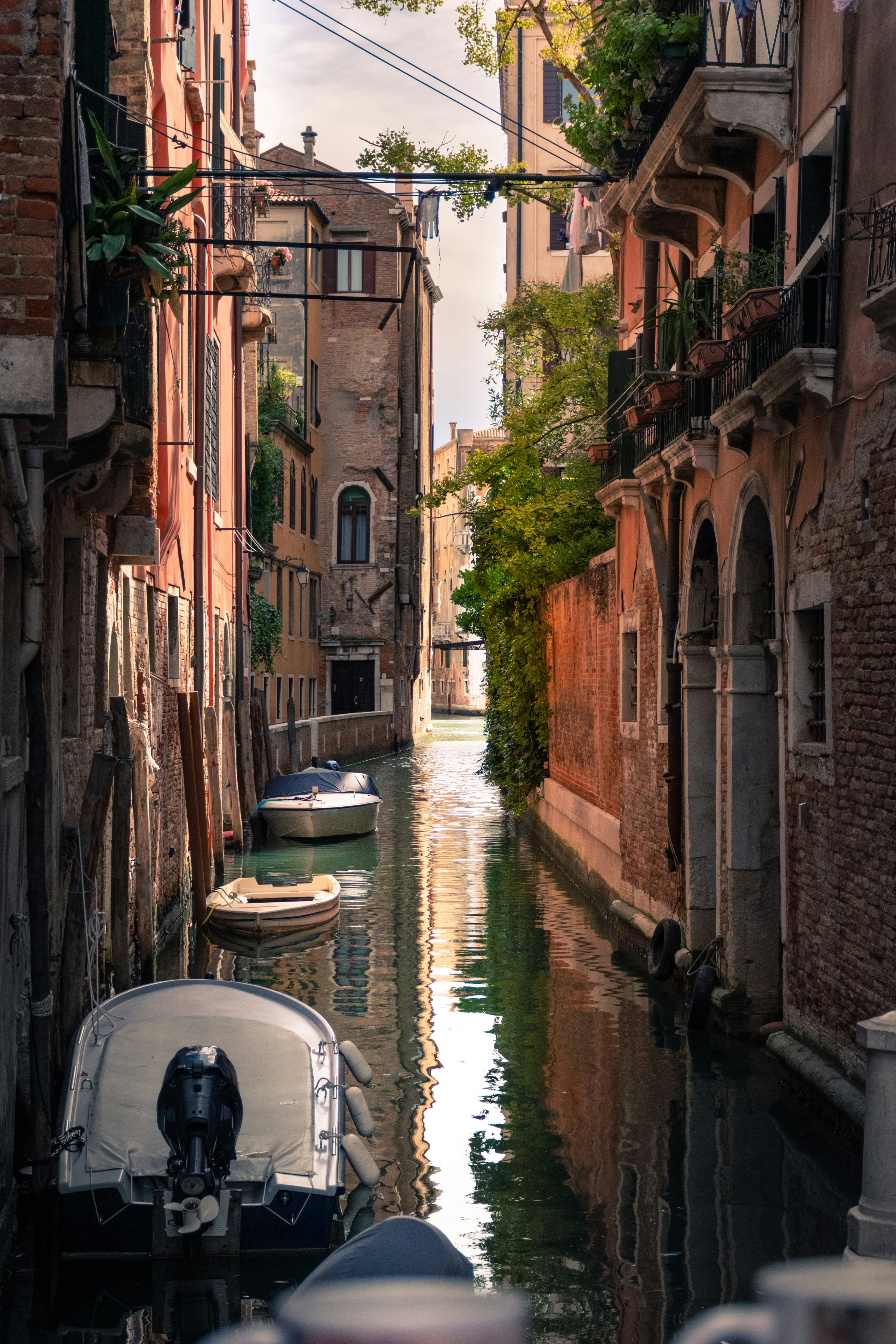 A water canal in Venice drifts in between buildings dotted with boats on a sunny day.