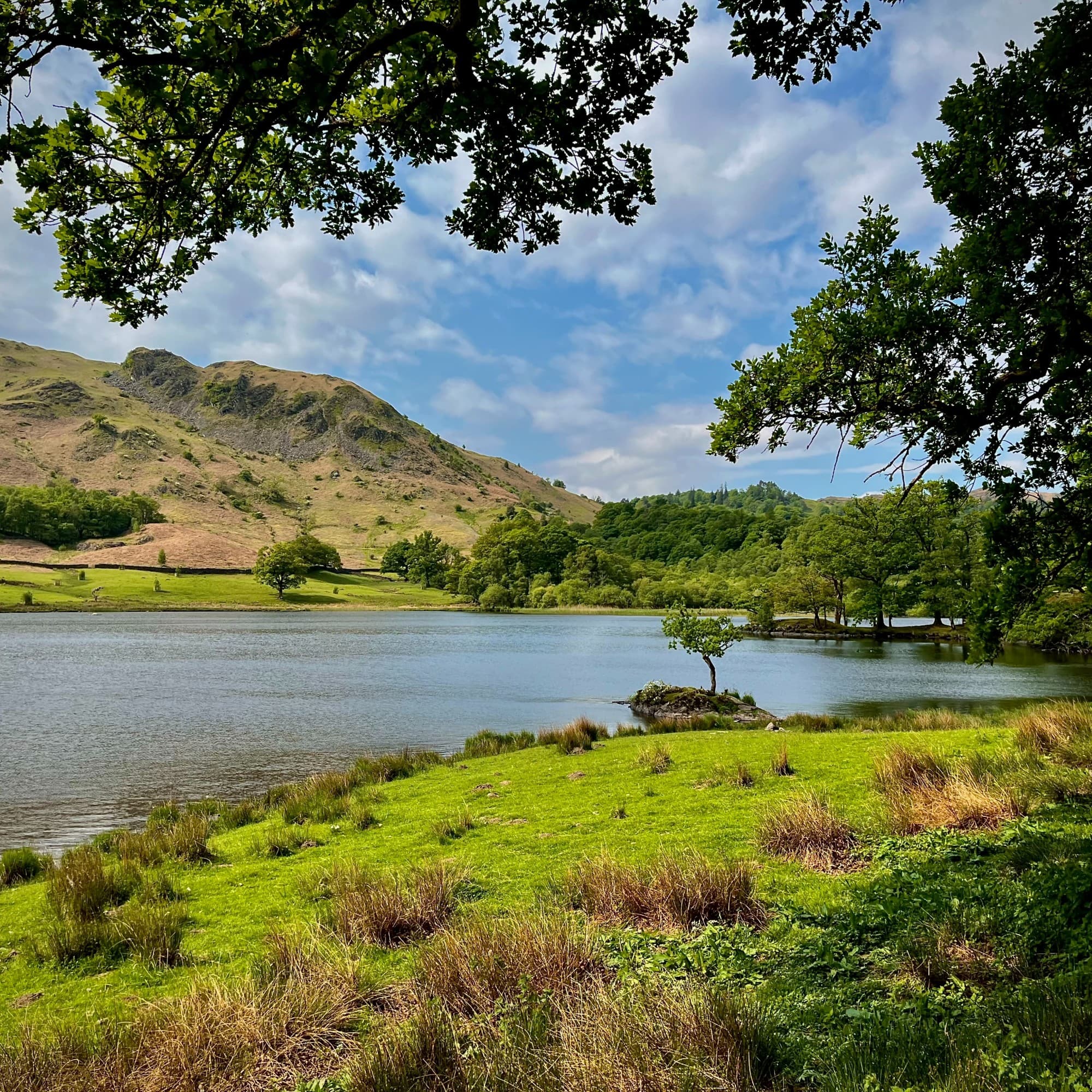 The image showcases a landscape featuring a lake surrounded by lush greenery and rolling hills under a partly cloudy sky.