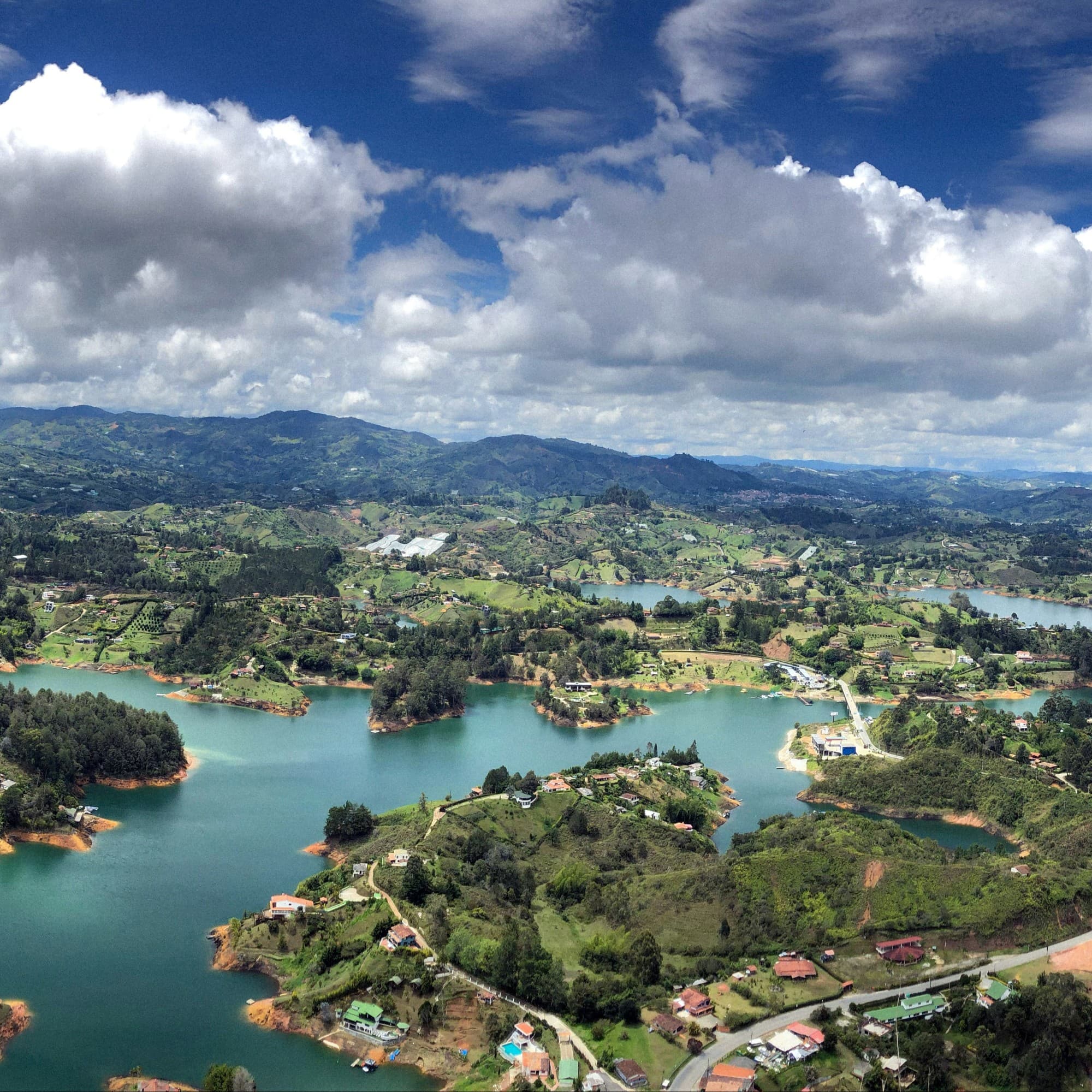 A panoramic view of a lush, green landscape with a winding road and multiple bodies of water surrounded by trees.