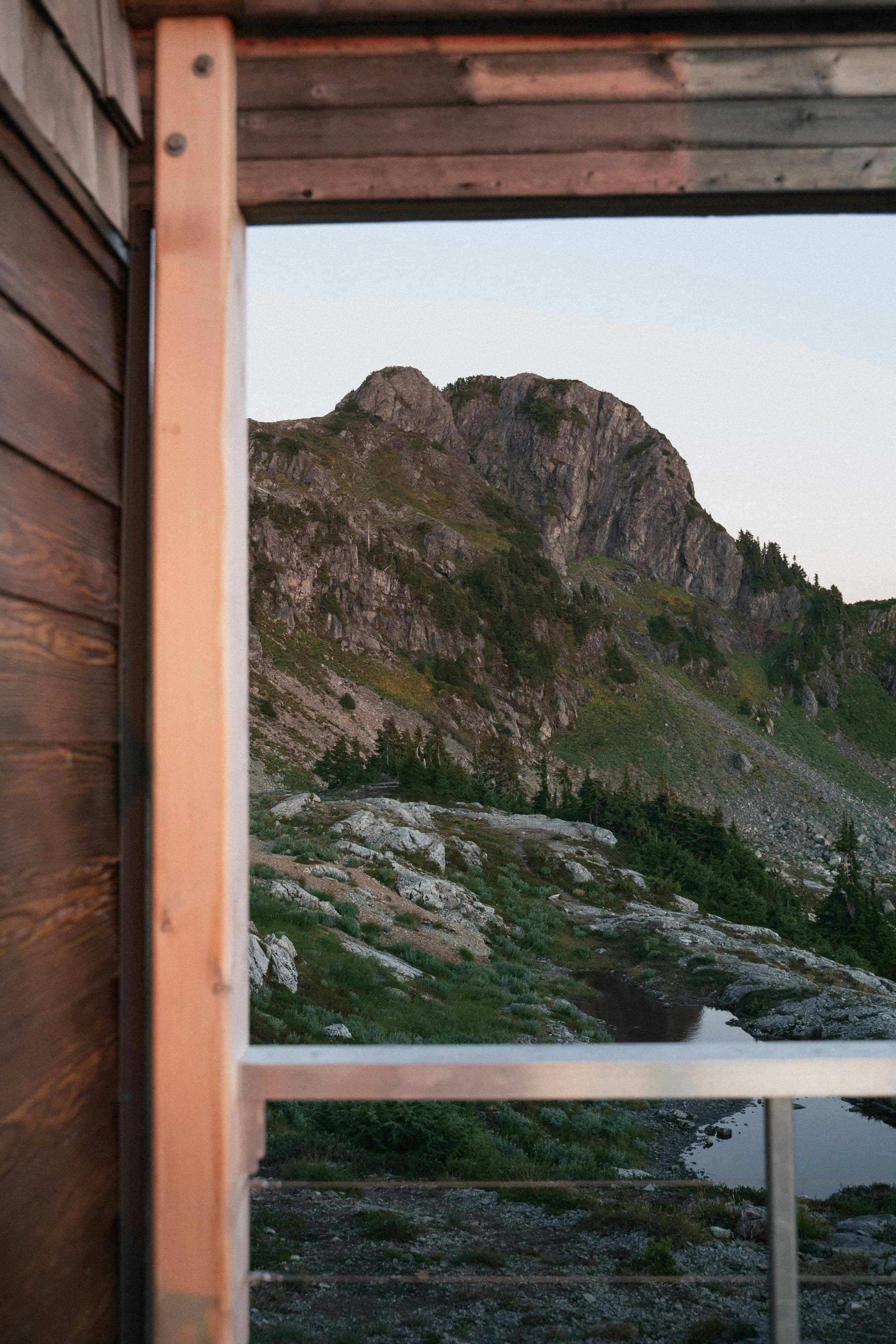 The image shows a mountainous landscape viewed through a window frame, highlighting the contrast between human structures and natural scenery.