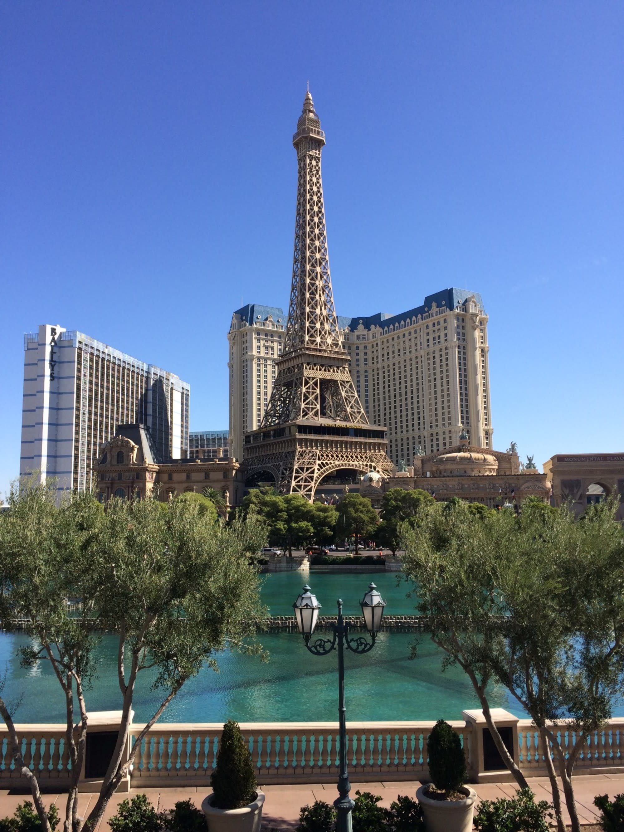 A picturesque replica of the Eiffel Tower by a calm body of water, flanked by greenery and Parisian-themed architecture.