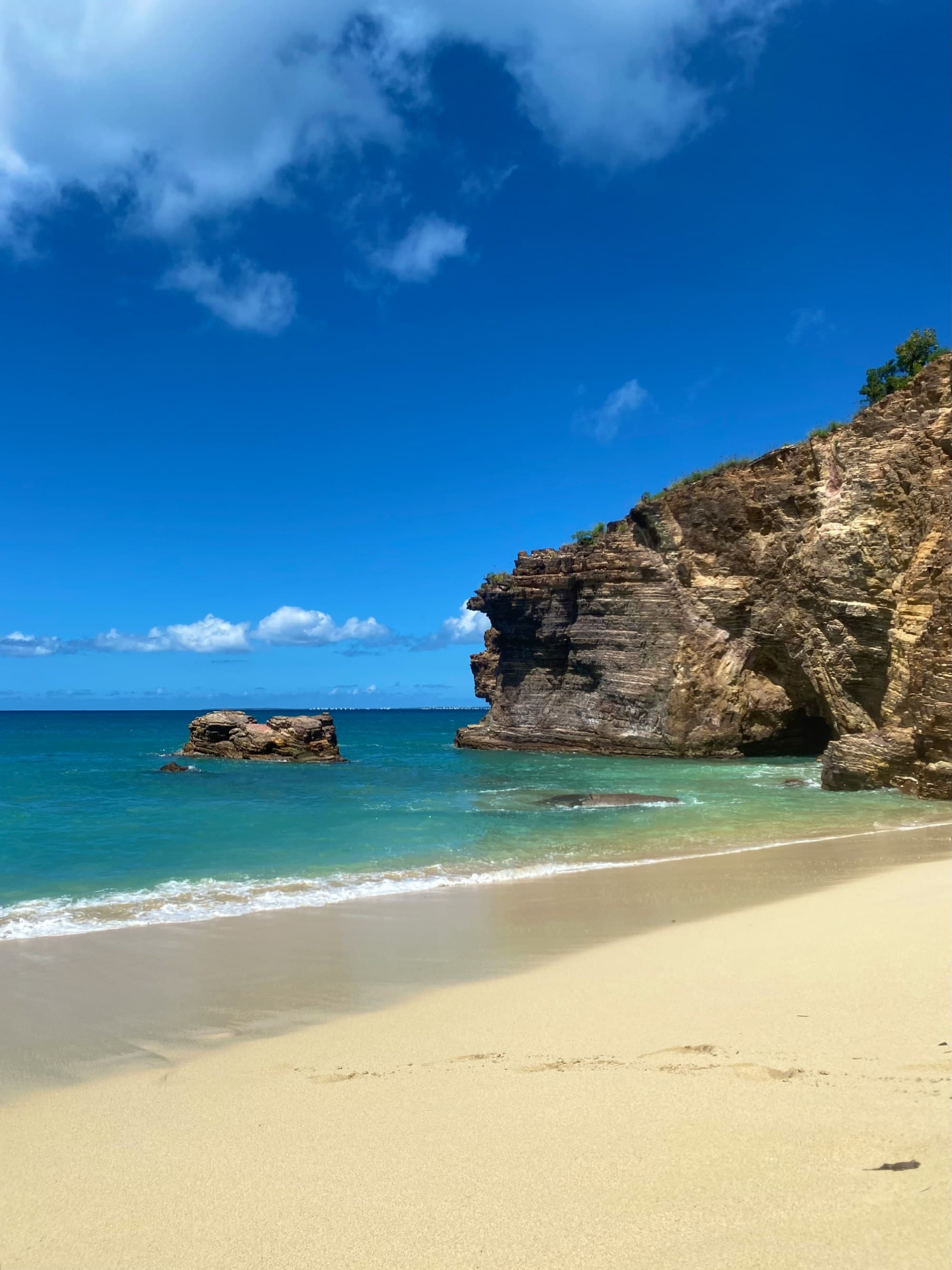 A tranquil beach scene with golden sands, a prominent rock formation, and clear blue skies over turquoise waters.