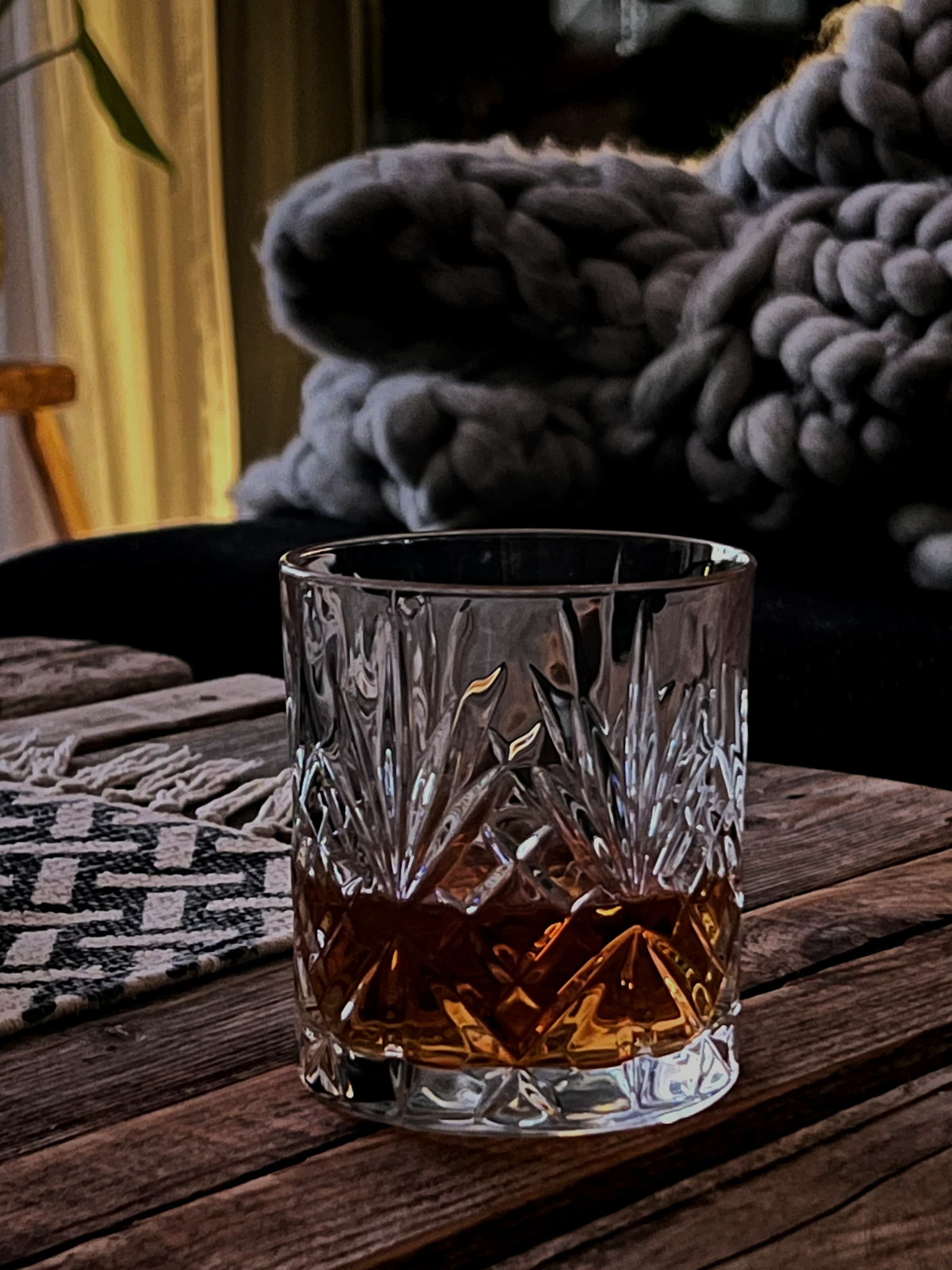 A rocks glass with whisky on a wooden table.