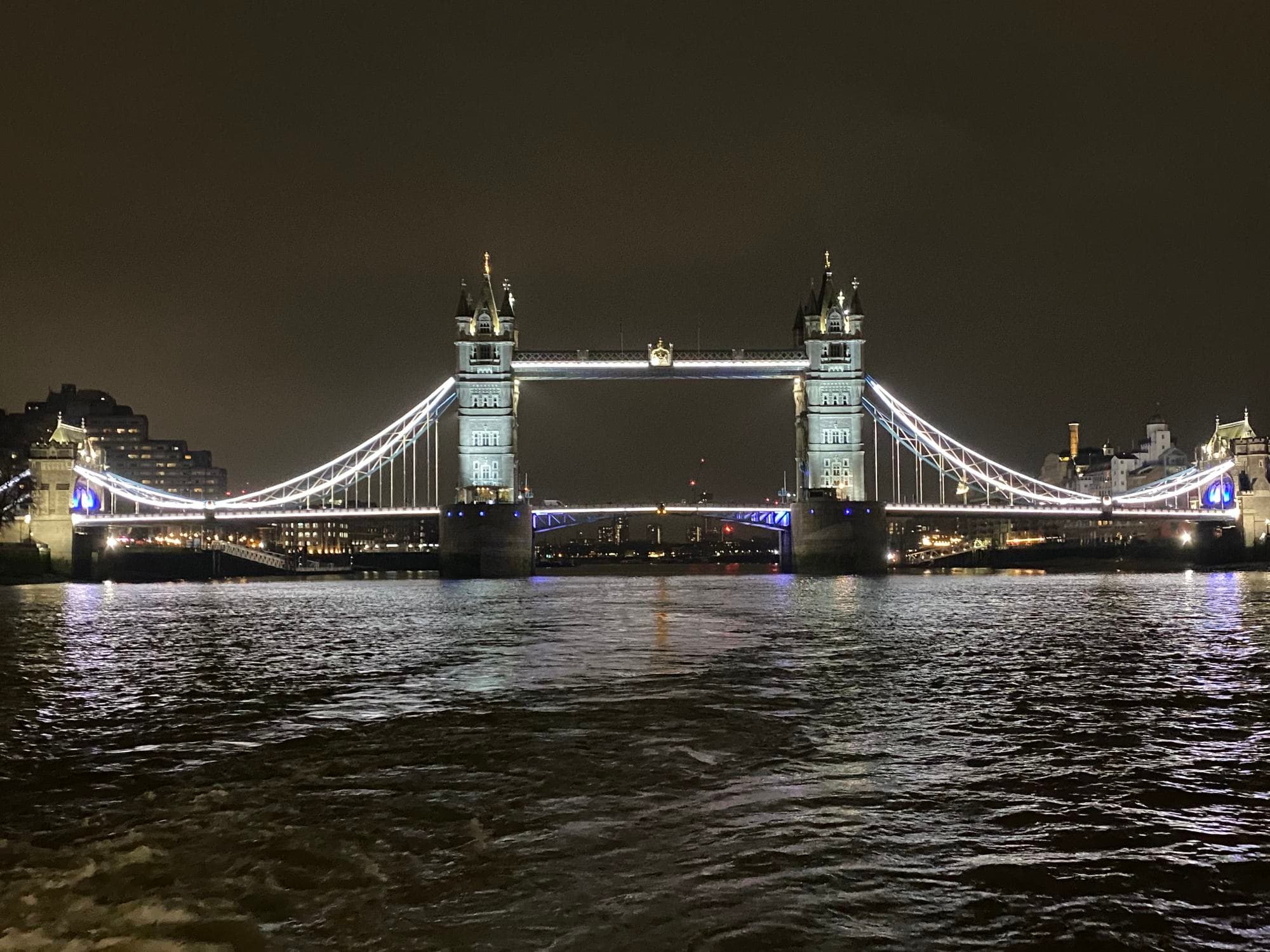 A view of the bridge in London lit up at night with the river in front.