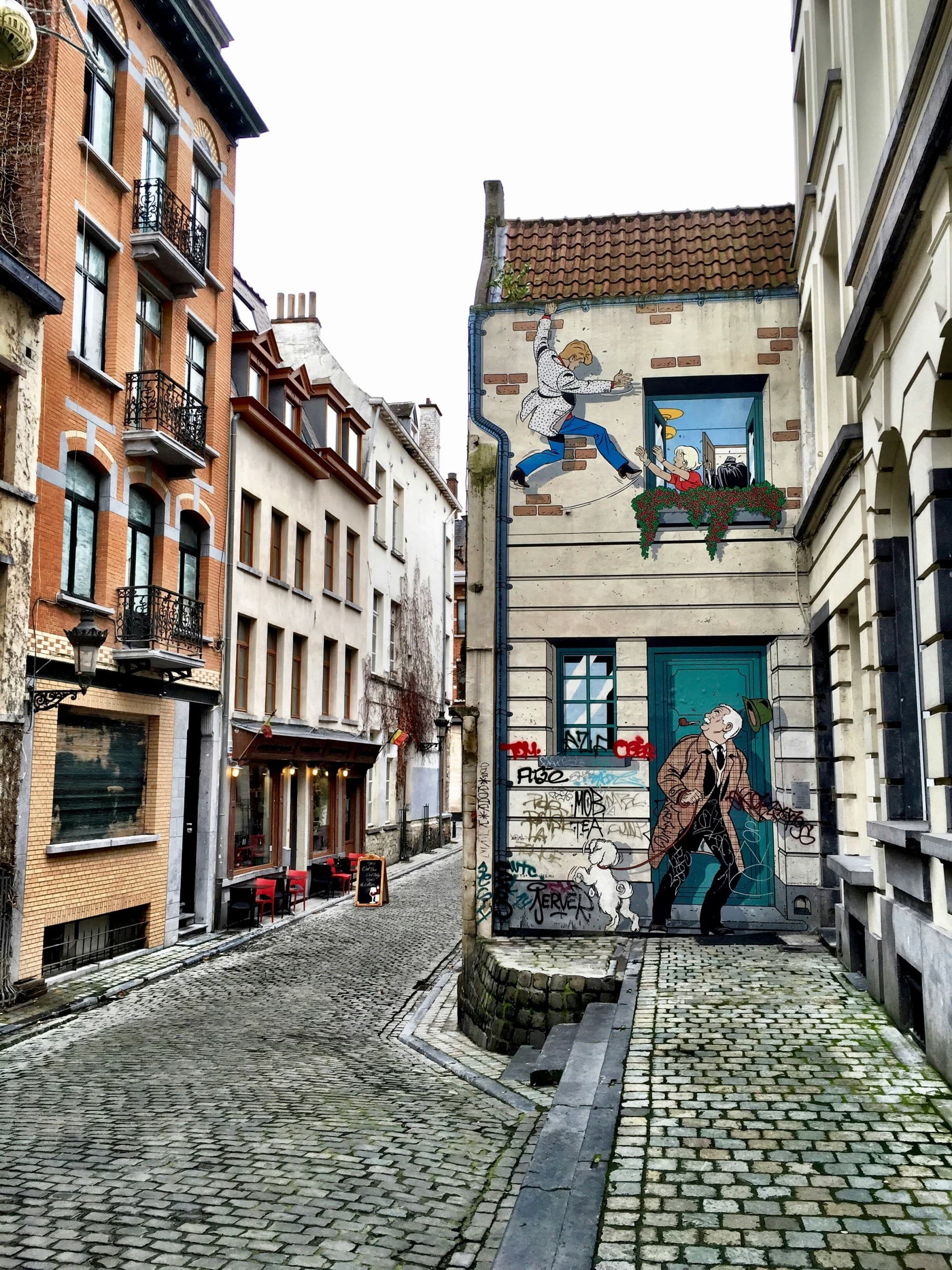 A brick street with houses with a lot of windows and painted murals in the surrounding areas.