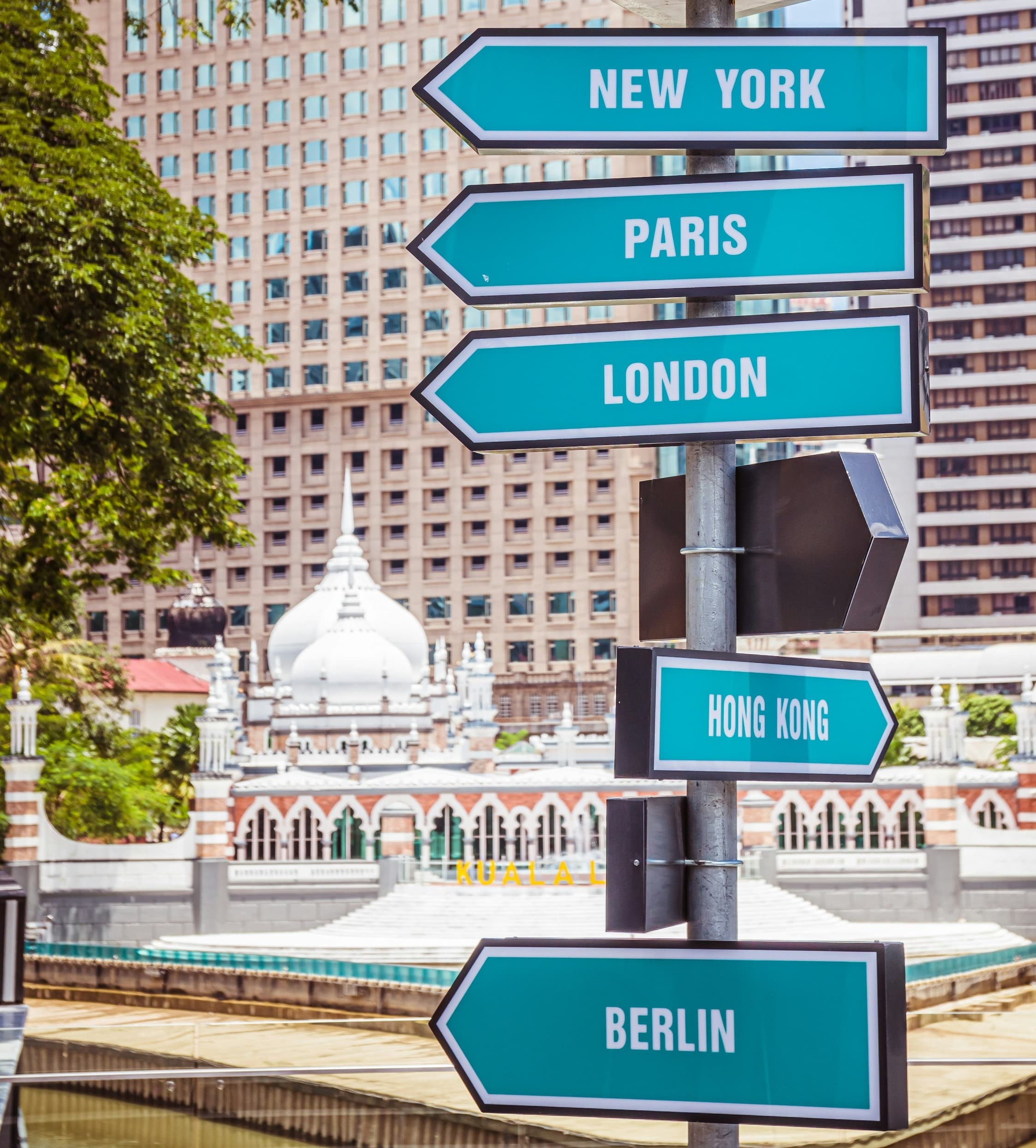 Direction signs in blue and white paint pointing to various destinations with buildings and trees in the background.