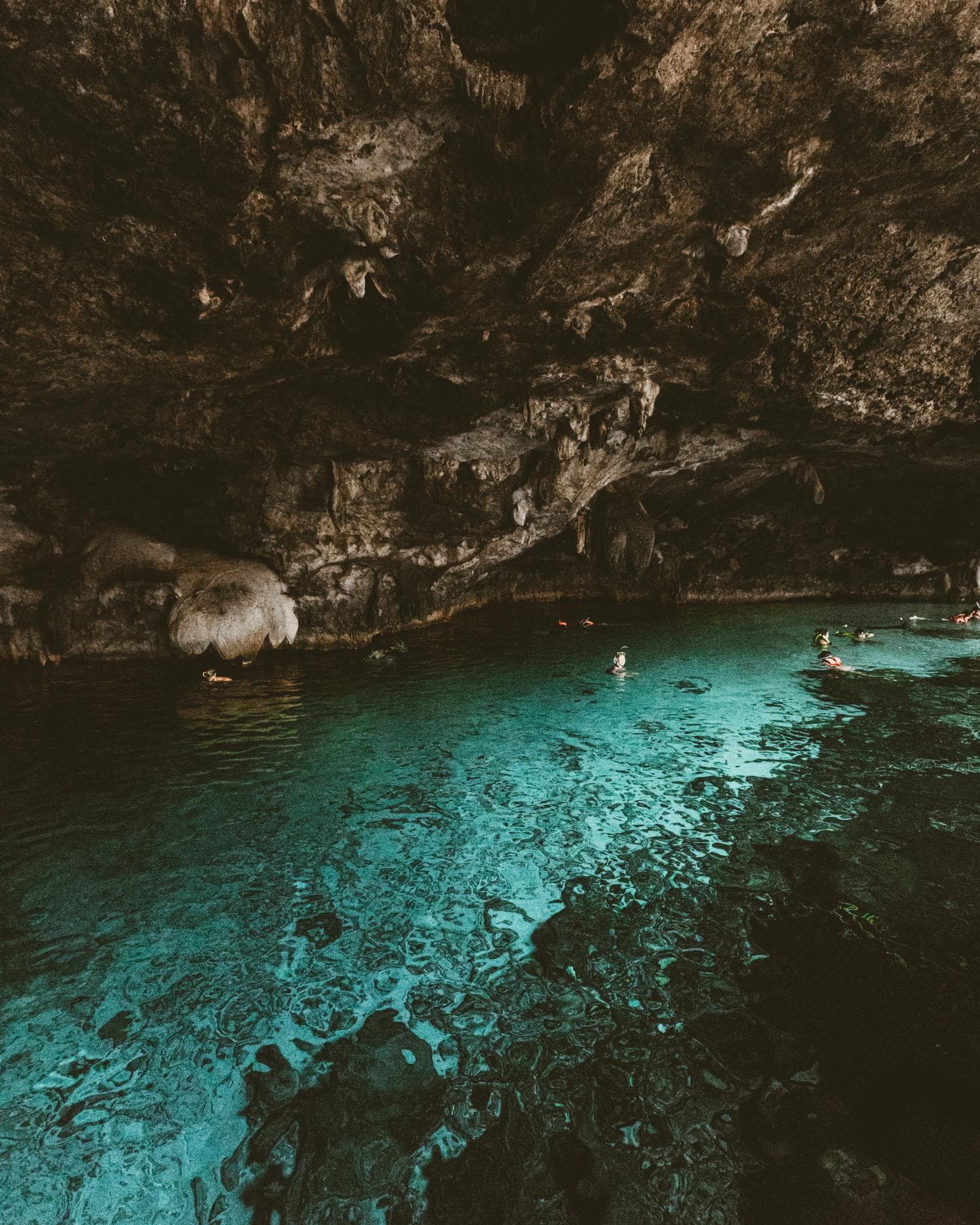 Cenote with natural light flowing through rocks, making the water glow blue.